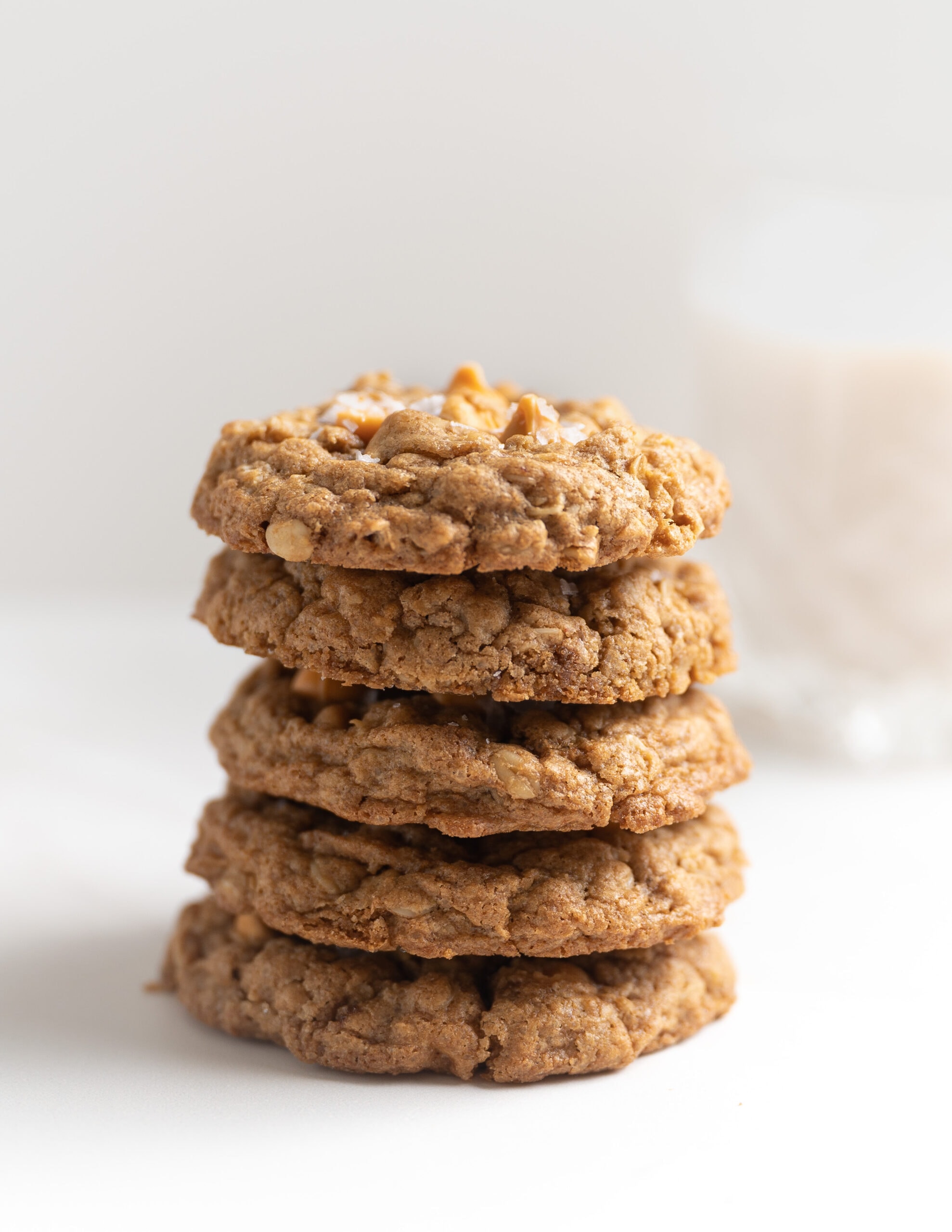 Four oatmeal butterscotch cookies stacked on top of one another with a glass of milk in the background.