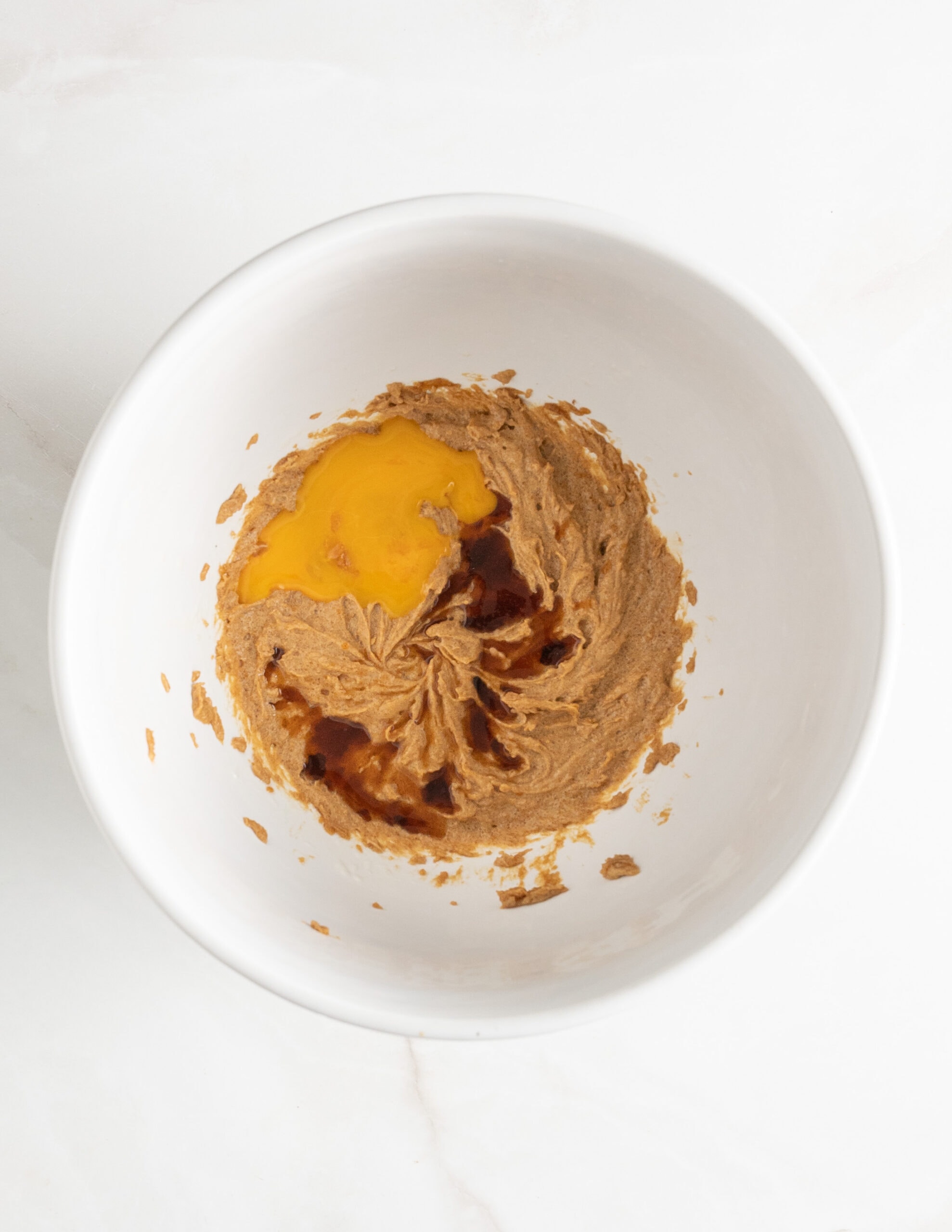 A large with bowl with an egg yolk, vanilla extract, melted butter and sugar.