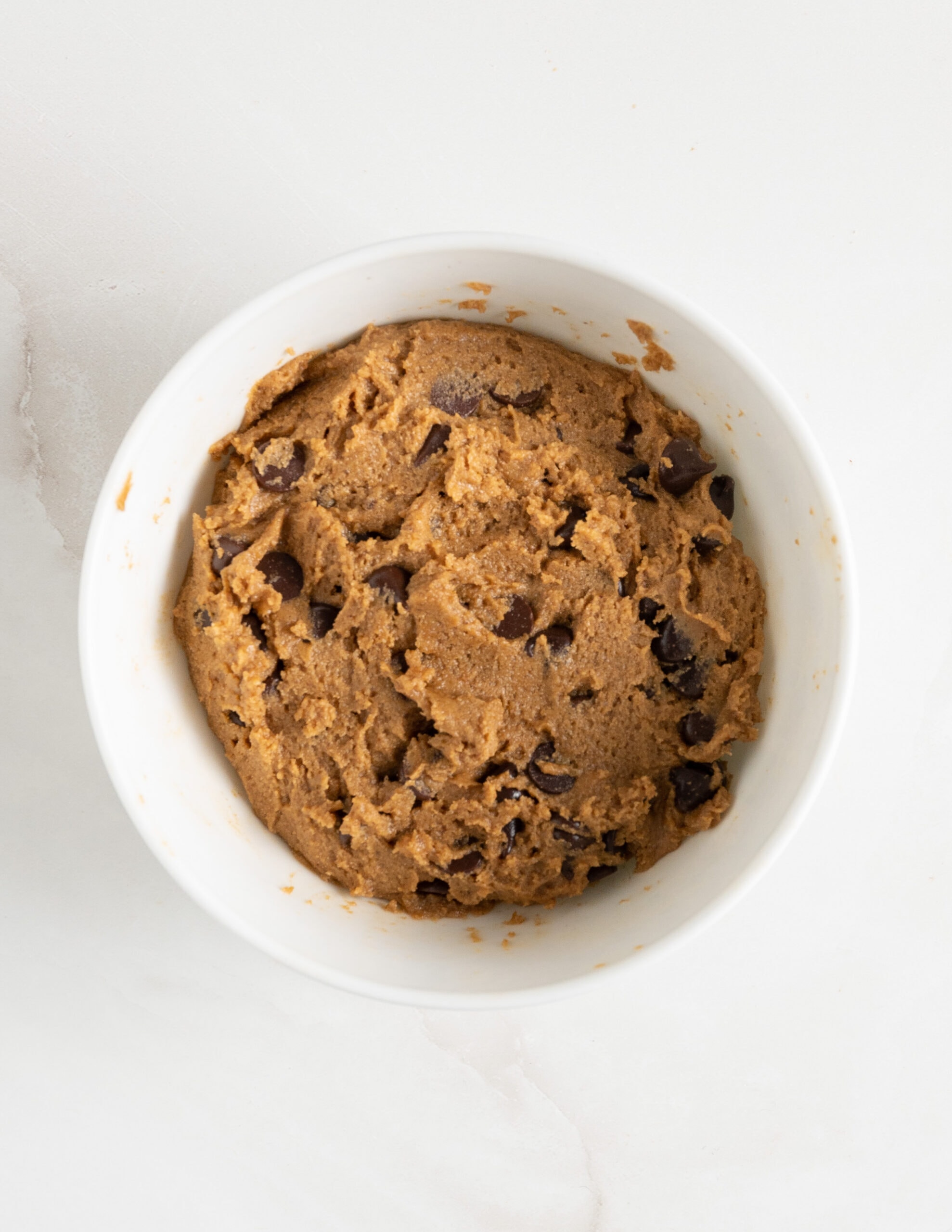 A large white bowl of pumpkin chocolate chip cookie dough. 