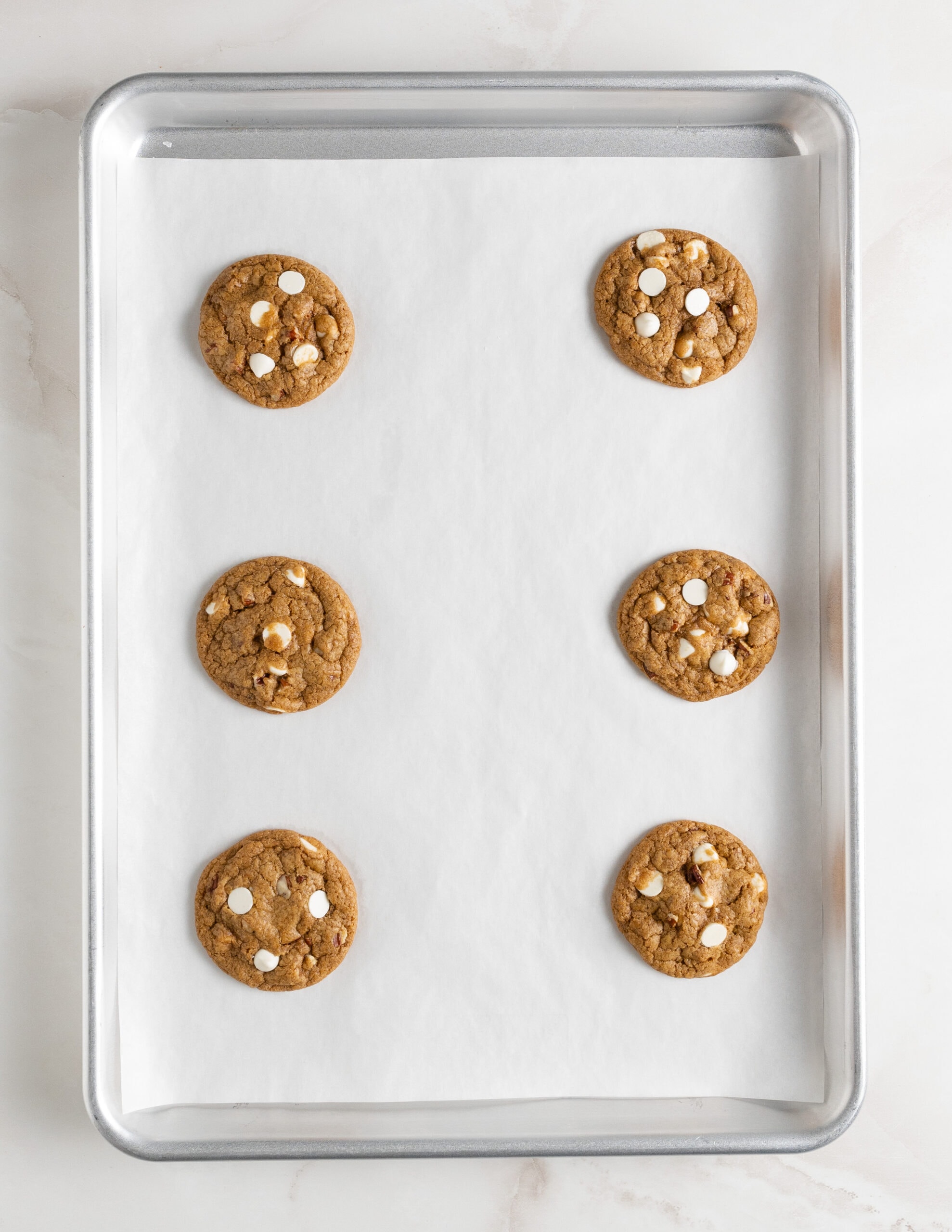 Large silver baking tray with white parchment paper and size white chocolate pumpkin pecan cookies baked. 