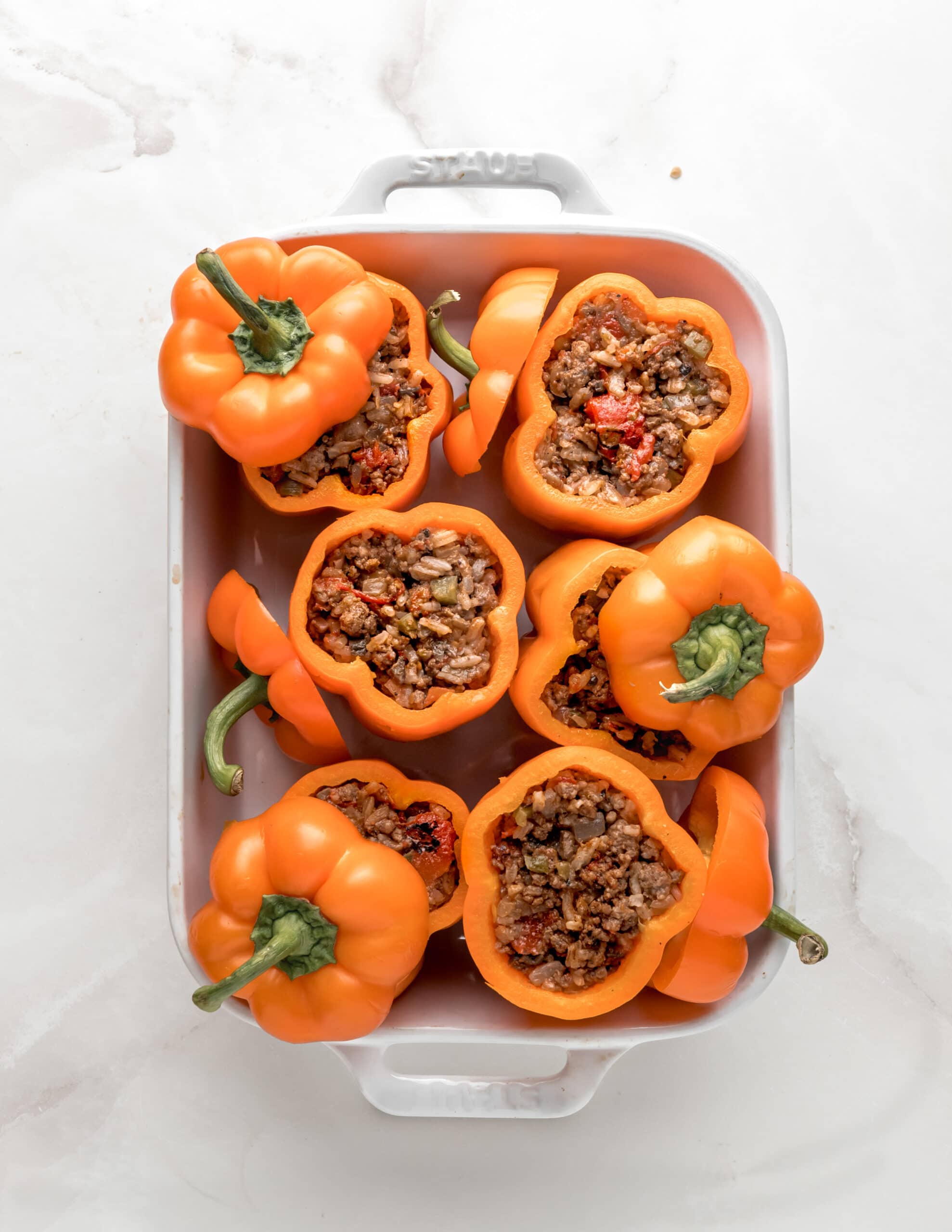 A large white ceramic baking dish with up-right orange bell  peppers stuffed with a meat mixture.