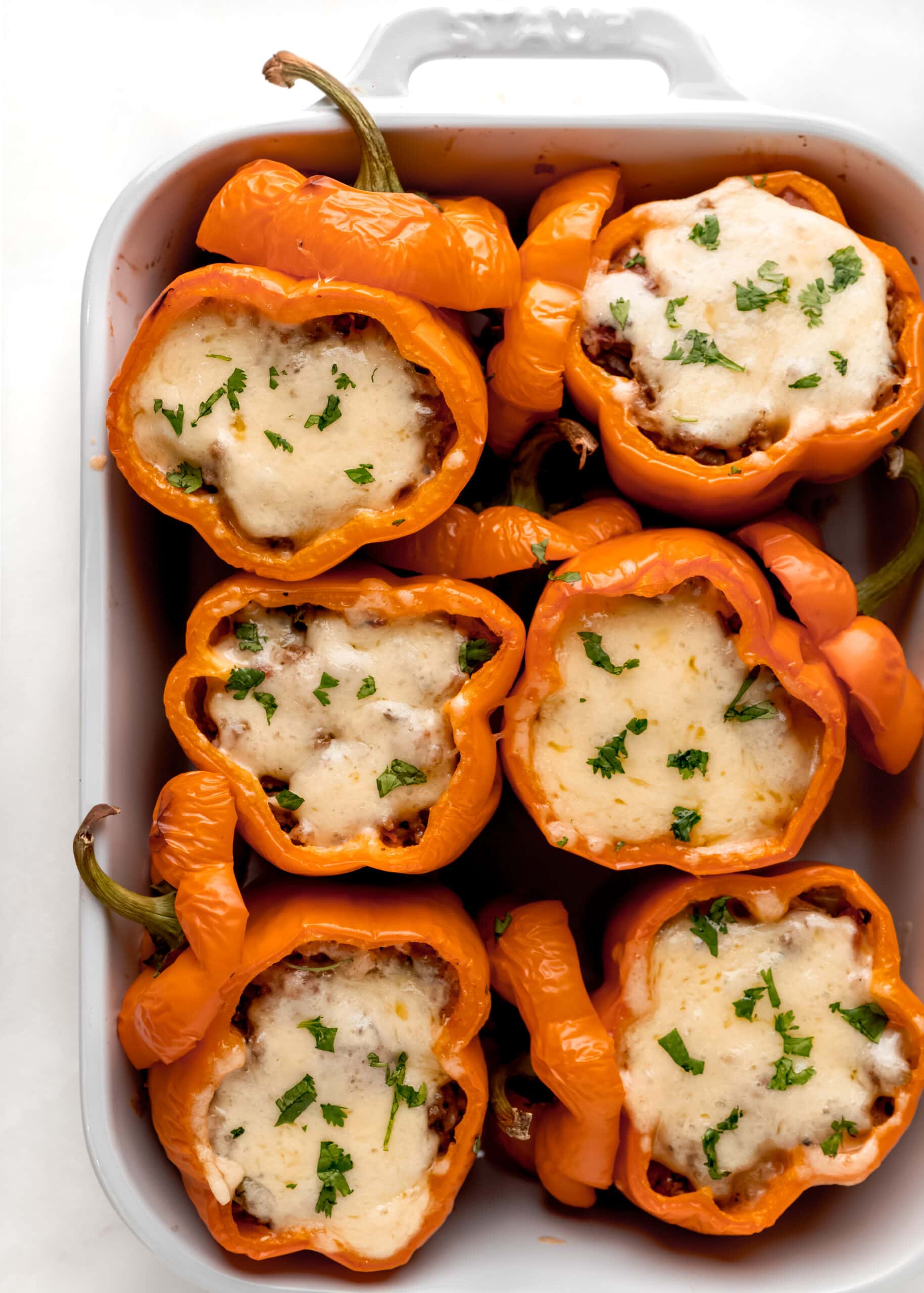 A large white baking dish, with stuffed orange peppers and melted cheese.