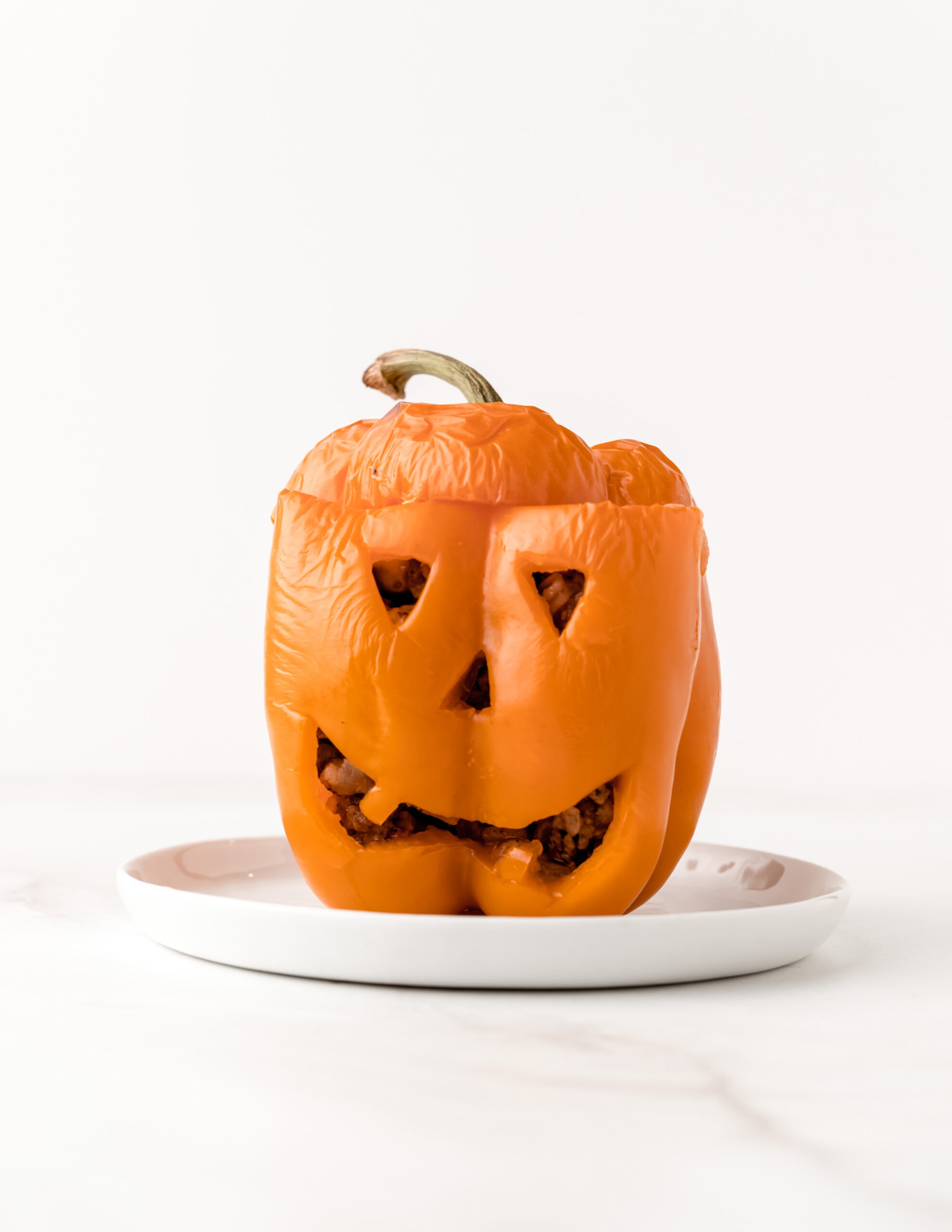 A picture of a gluten-free orange stuffed pepper with a jack-o-lantern face on a white plate.