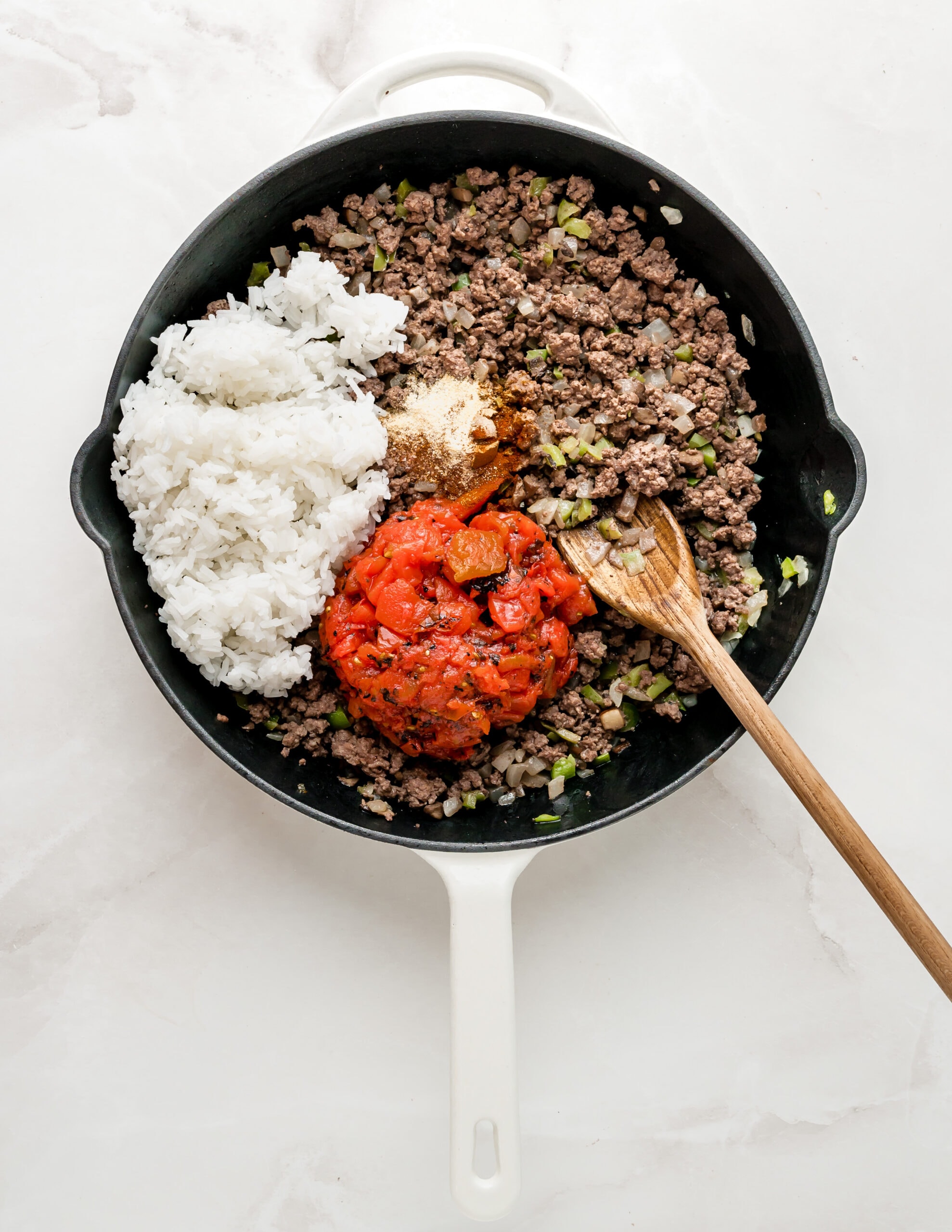 A large white skillet with ground beef, vegetables, cooked white rice, and fire-roasted tomatoes.