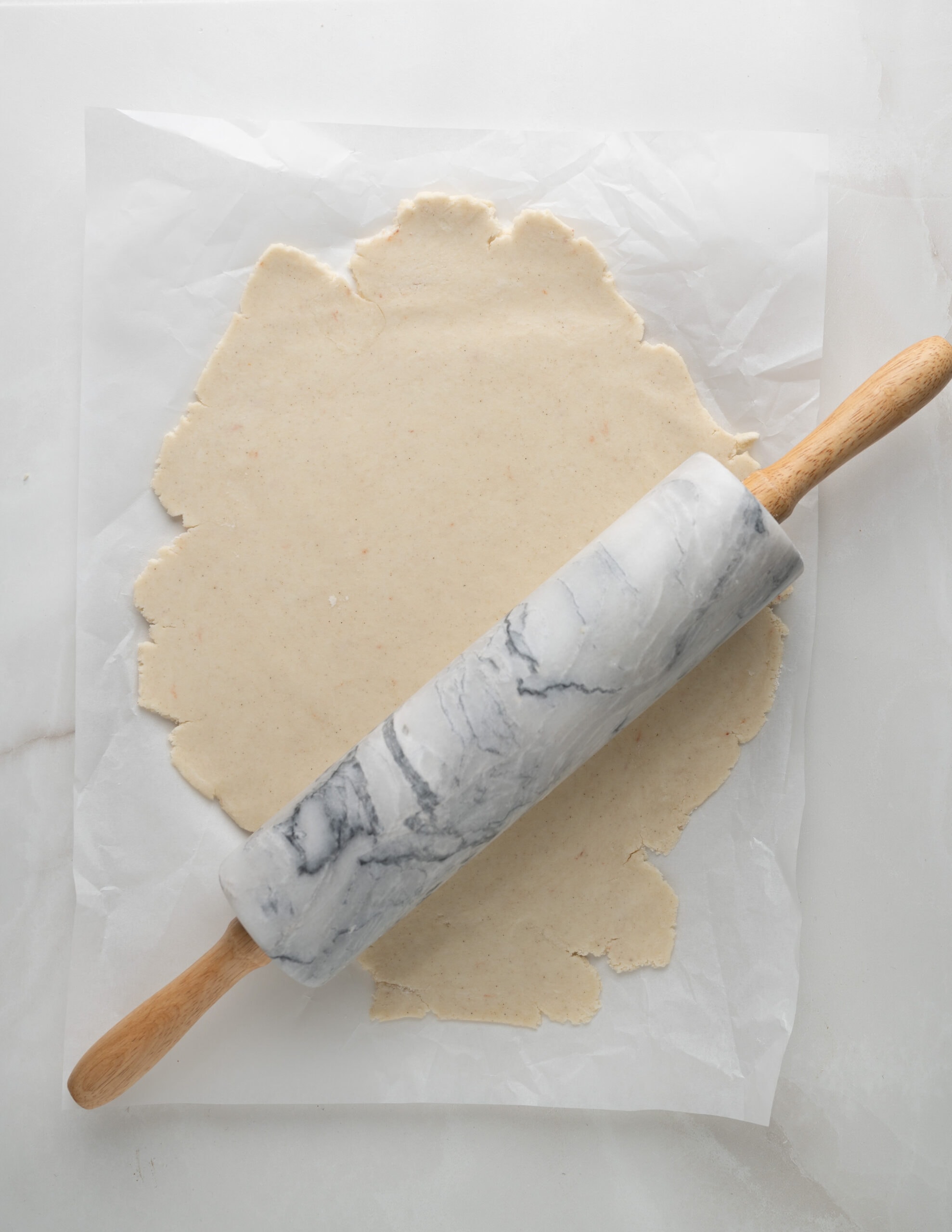 Pastry dough on a large piece of parchment paper, rolled out with a marble style rolling pin. 
