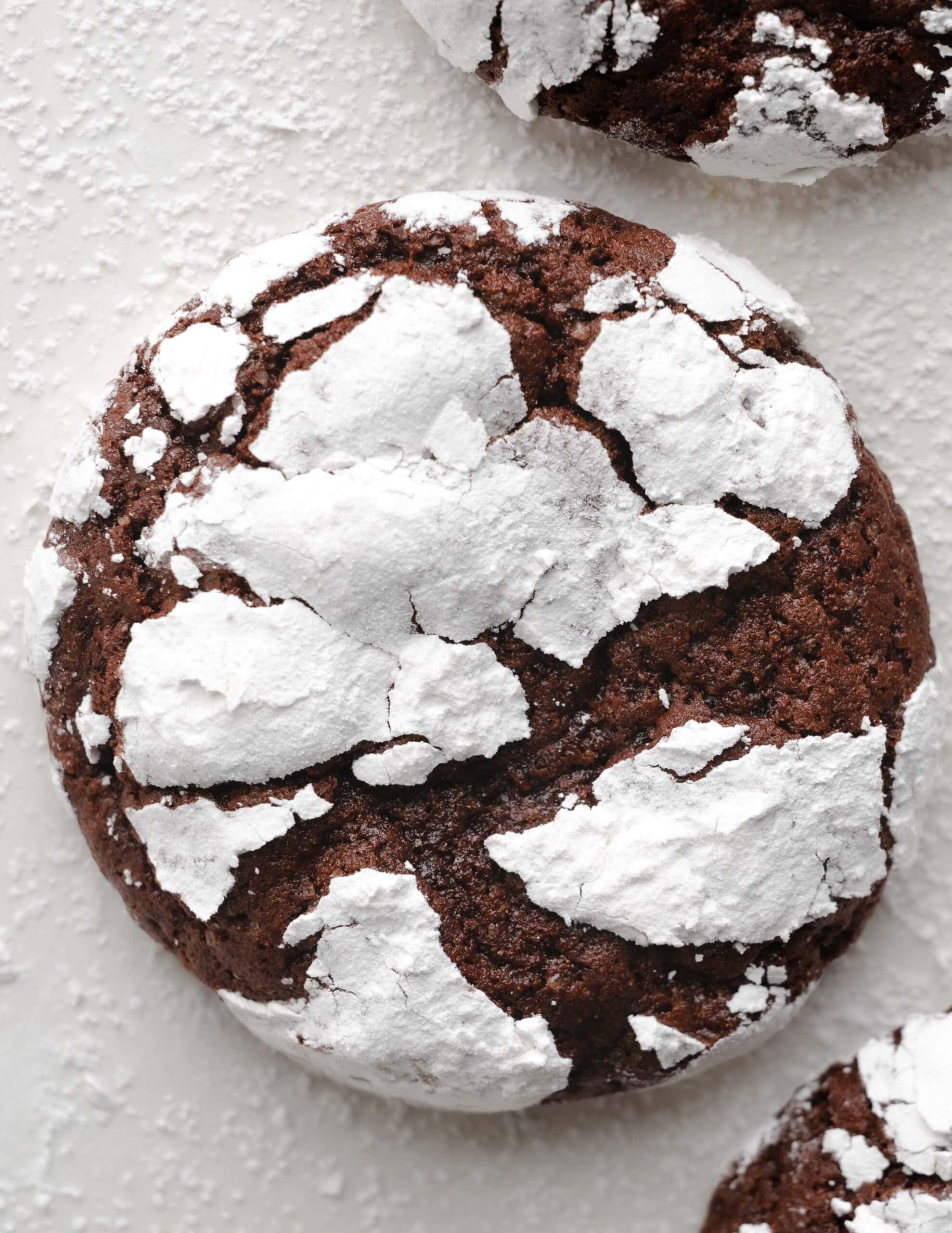 A large gluten-free chocolate crinkle cookies with a dusting powder powdered sugar, and two chocolate cookies in each opposite corner.
