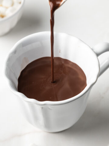 A zoomed in photo of oat milk hot chocolate being poured into a white ceramic mug.
