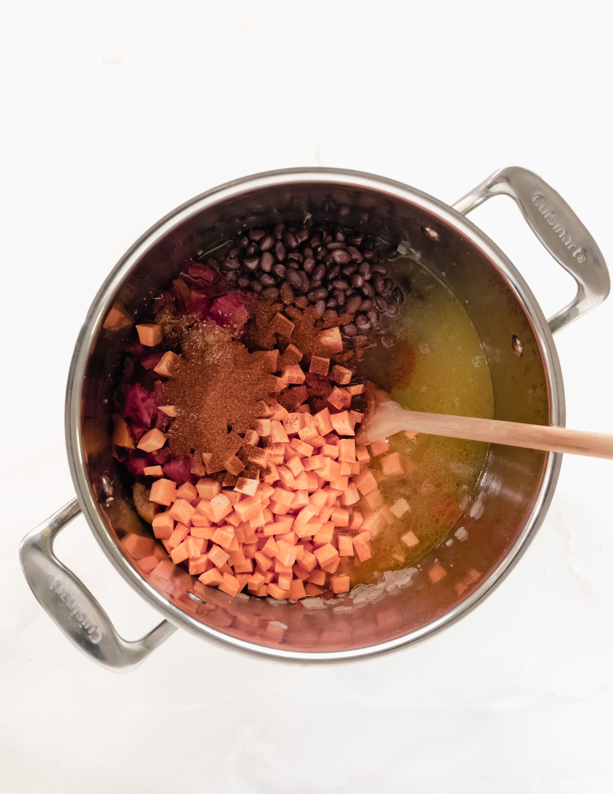Large stainless steel pot in sweet potatoes, black beans, spices, ground beef, and tomatoes, stirred with a wooden spoon.