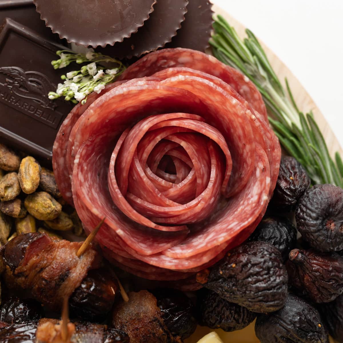 Salami Rose on a charcuterie board with dates, pistachios, dried figs, chocolate, babys breath, and rosemary