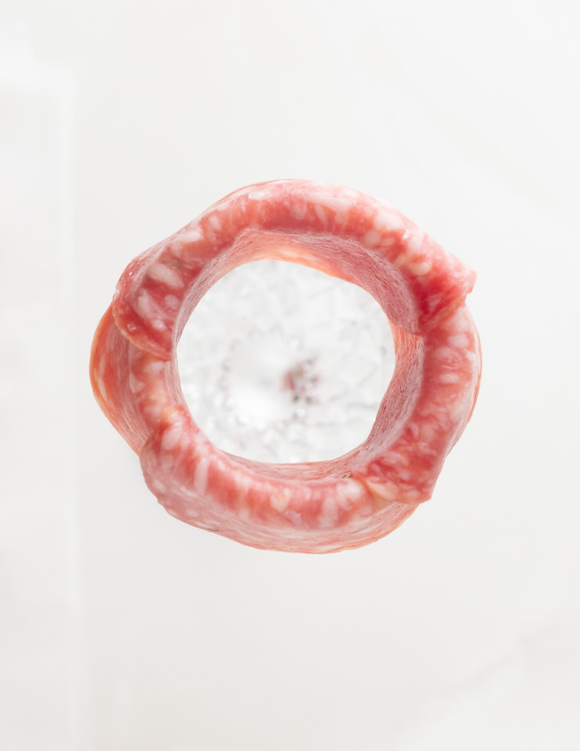 An aerial view on slice salami covering the rim of the champagne flute. 