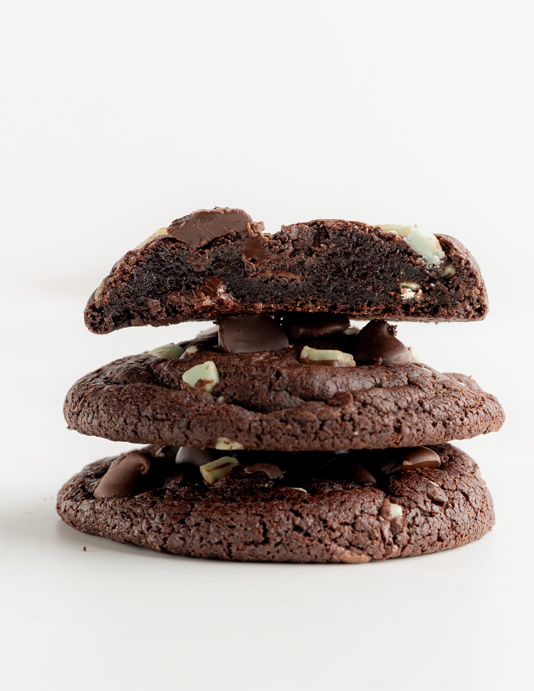 A stack of three chocolate mint cookies, with the top cookies slices in half to see the fudgy center.