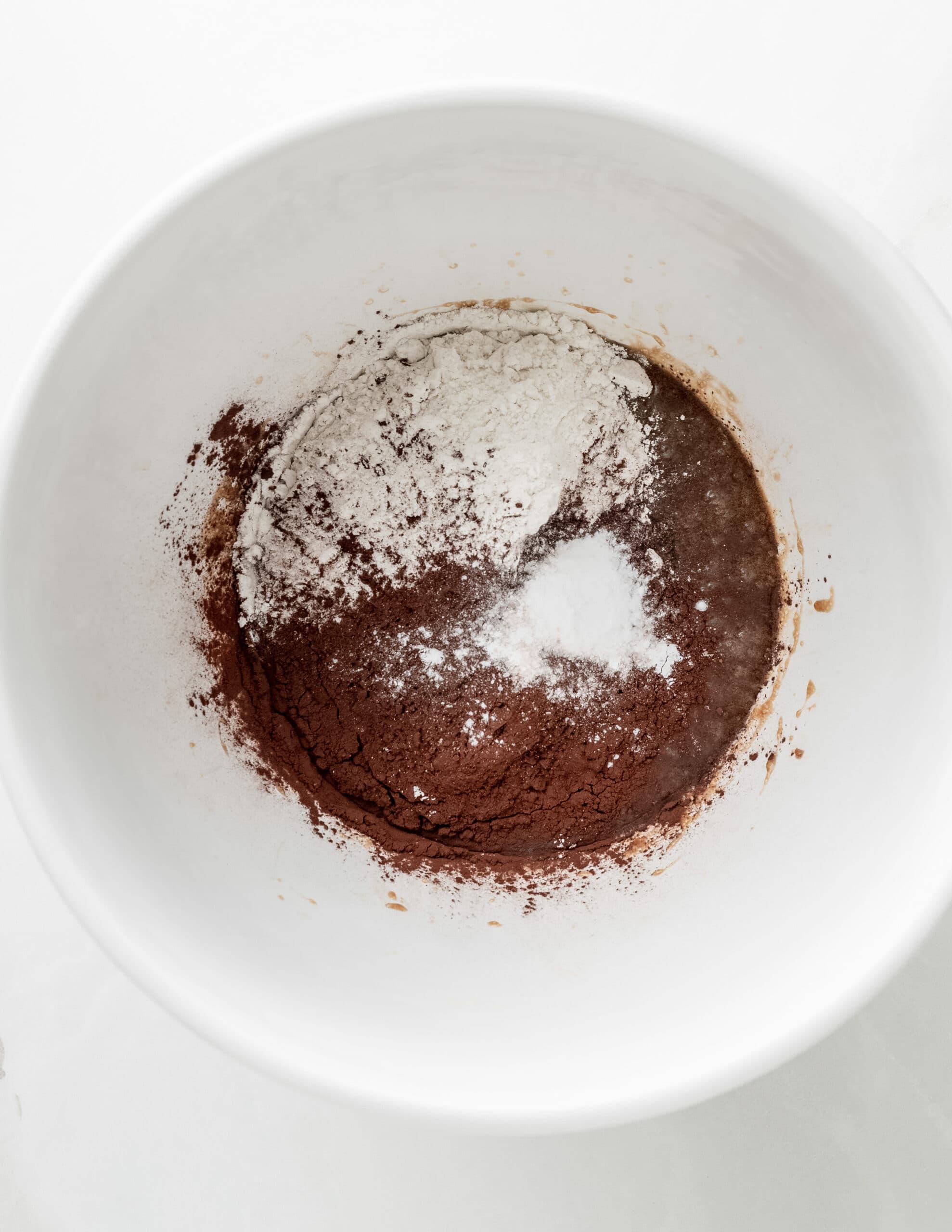 A large white bowl with cocoa powder, and flour adding to the wet ingredients.