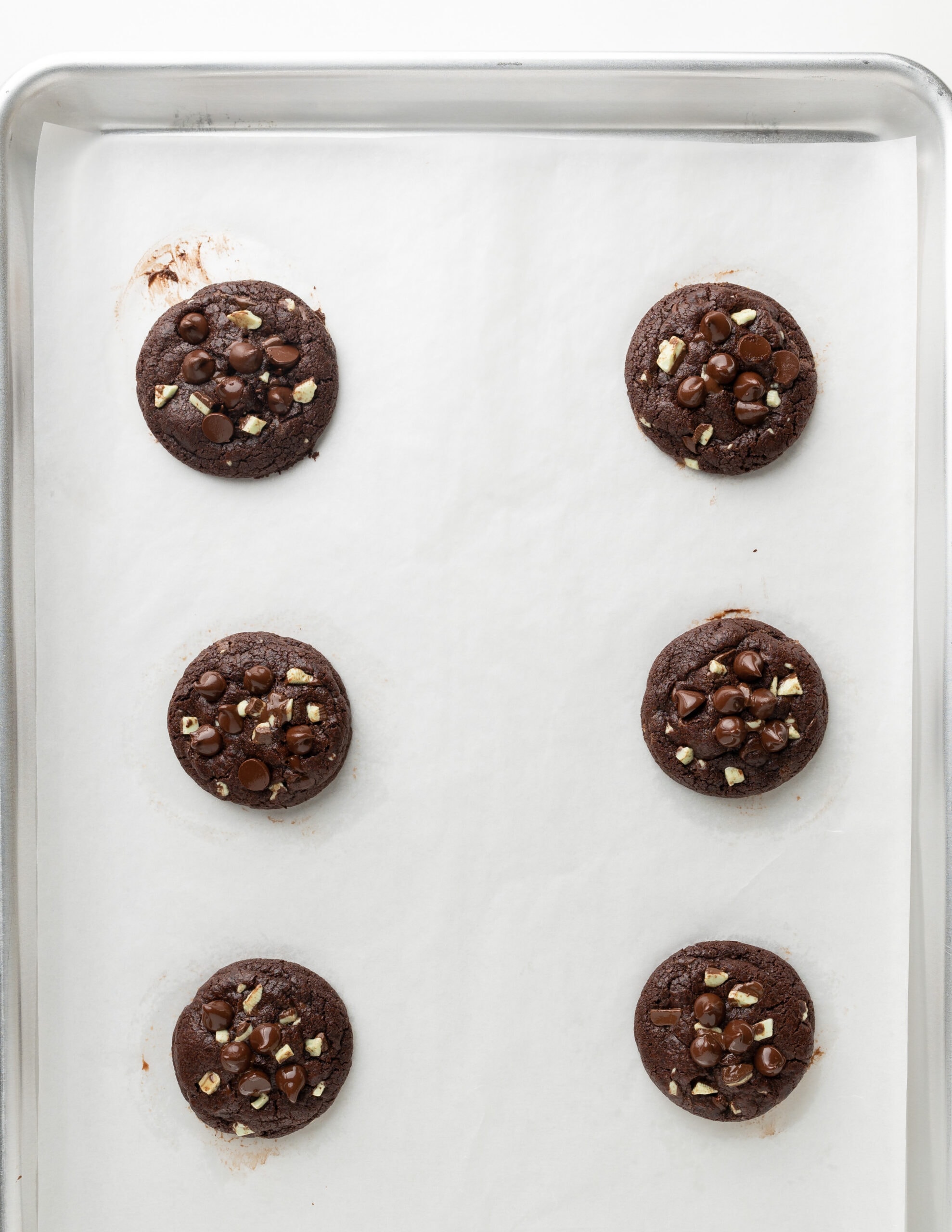 A large silver baking tray with freshly baked chocolate mint cookies right out of the oven with melty chocolate on top. 
