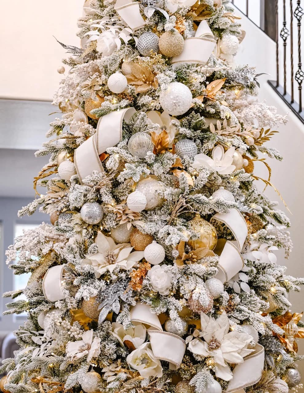 A close up picture of a white and gold christmas tree with white and gold ornaments and white ribbons throughout. 