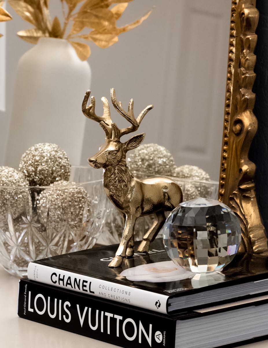 A brass decorative deer with gold ornaments in the back, a crystal oribe to the side of the deer, and two designer black books.