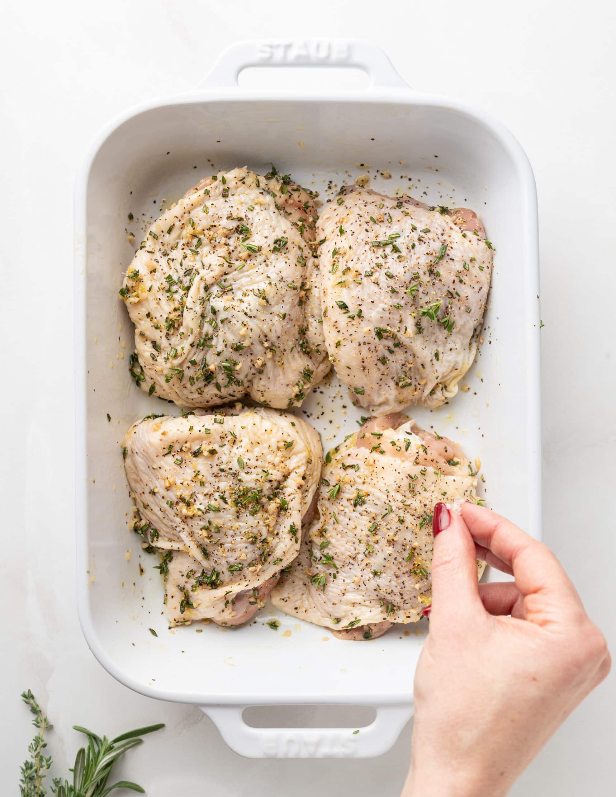 White rectangular skillet, with chicken thighs and herbs.