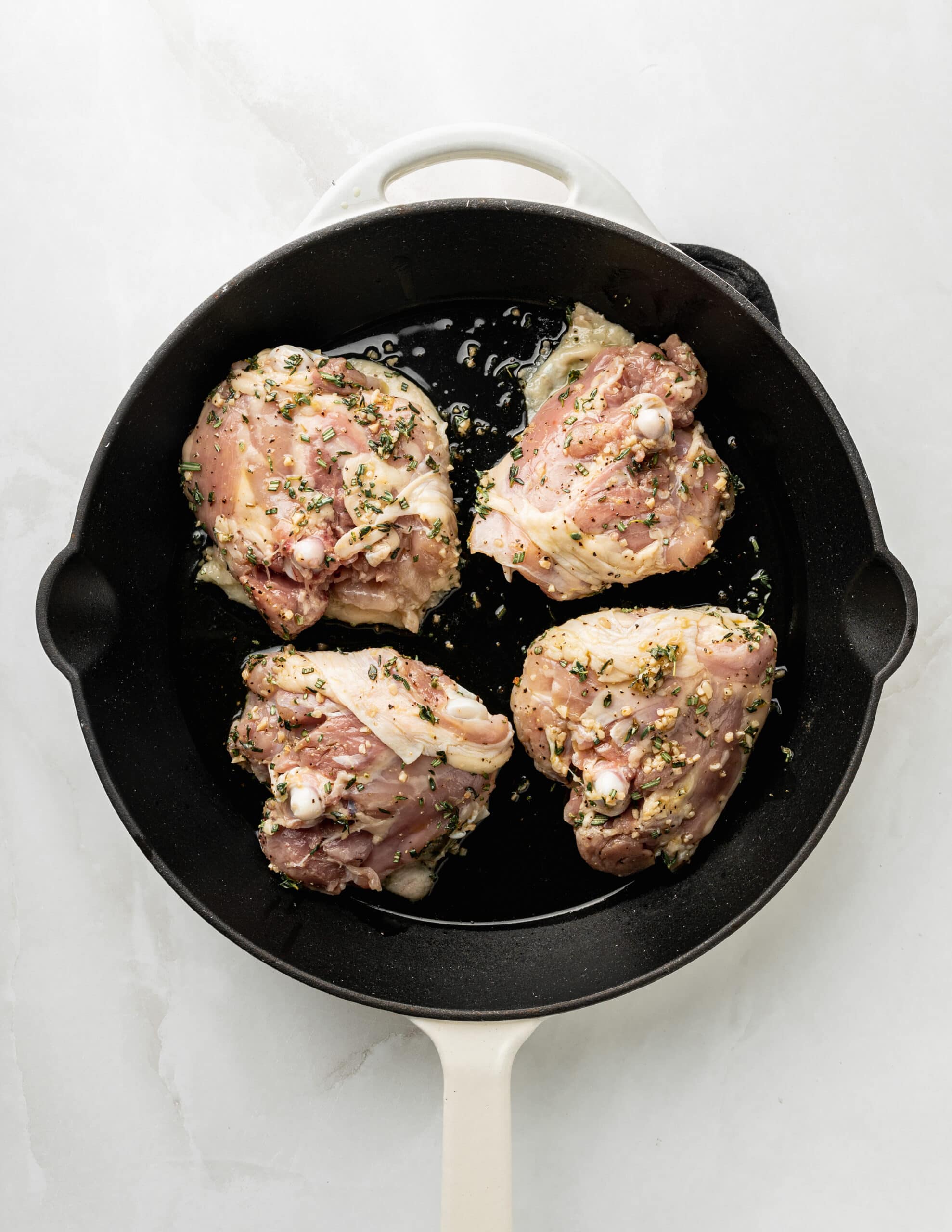Large white skillet with four chicken thighs.