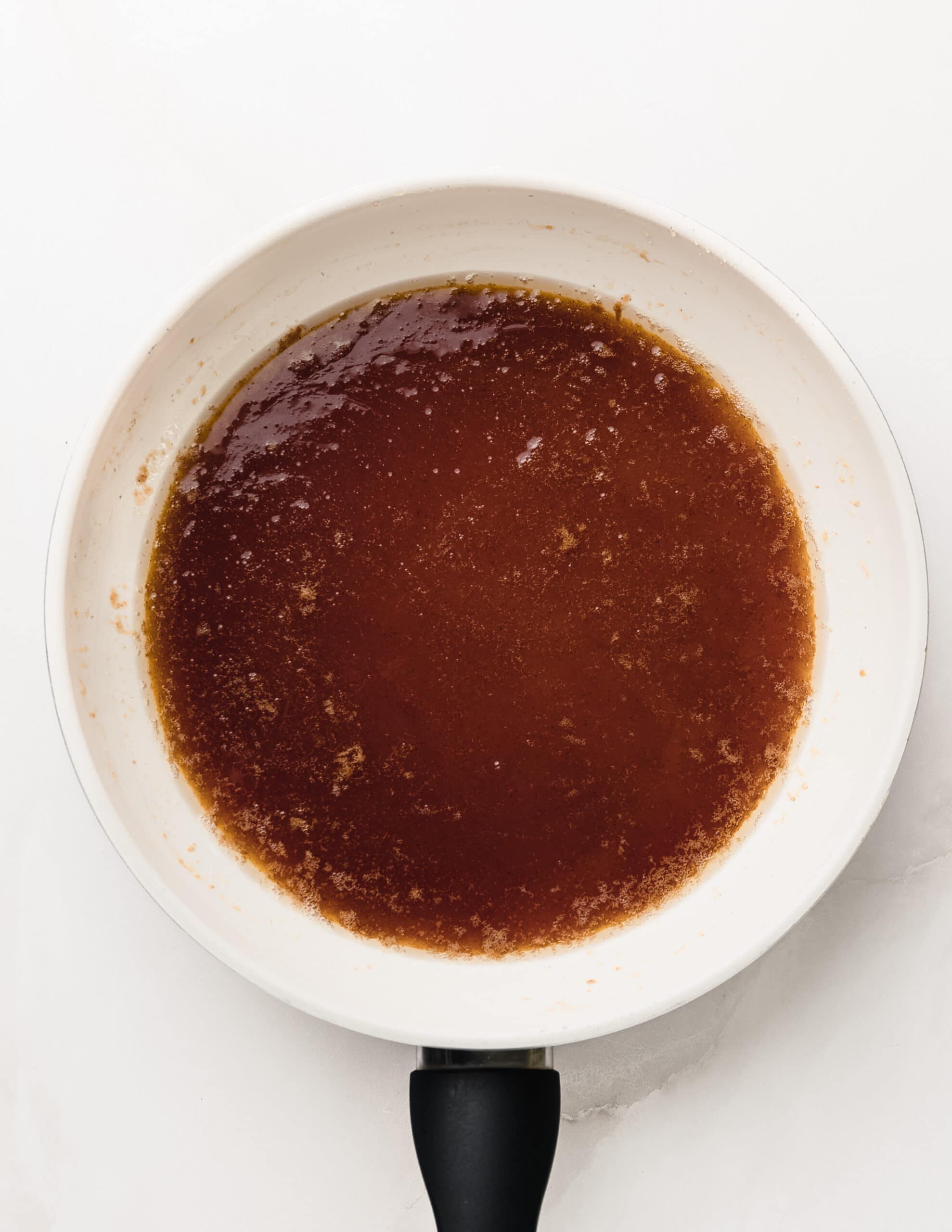 A picture of a white frying pan with brown butter, maple syrup, and honey.