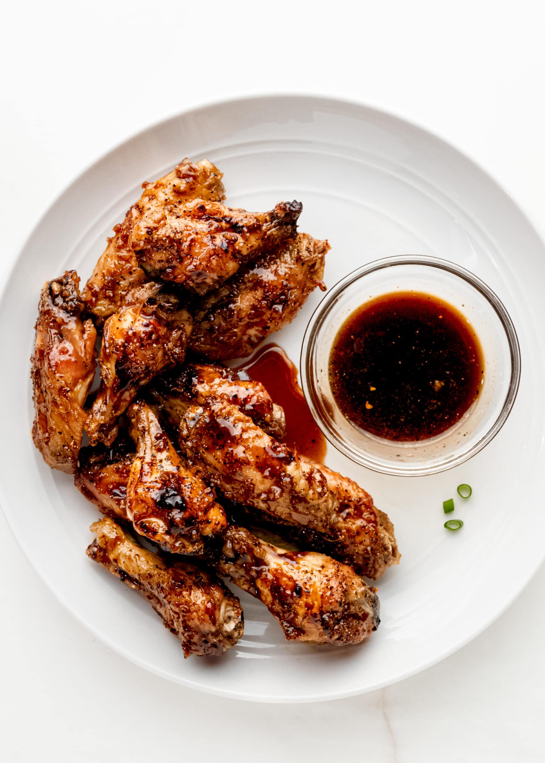 A white round plate with honey garlic chicken wings and a soy ginger sauce.