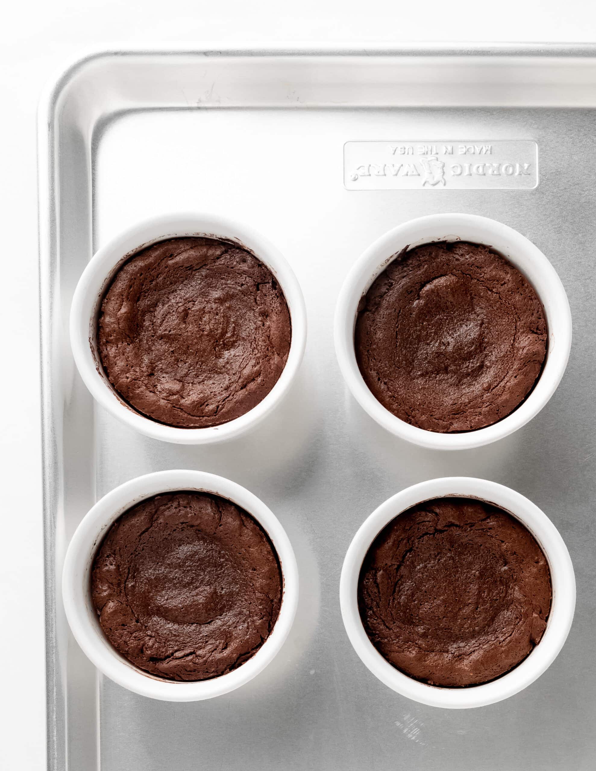 A metal tray with four fully baked molten lava cakes in white ceramic ramekins.