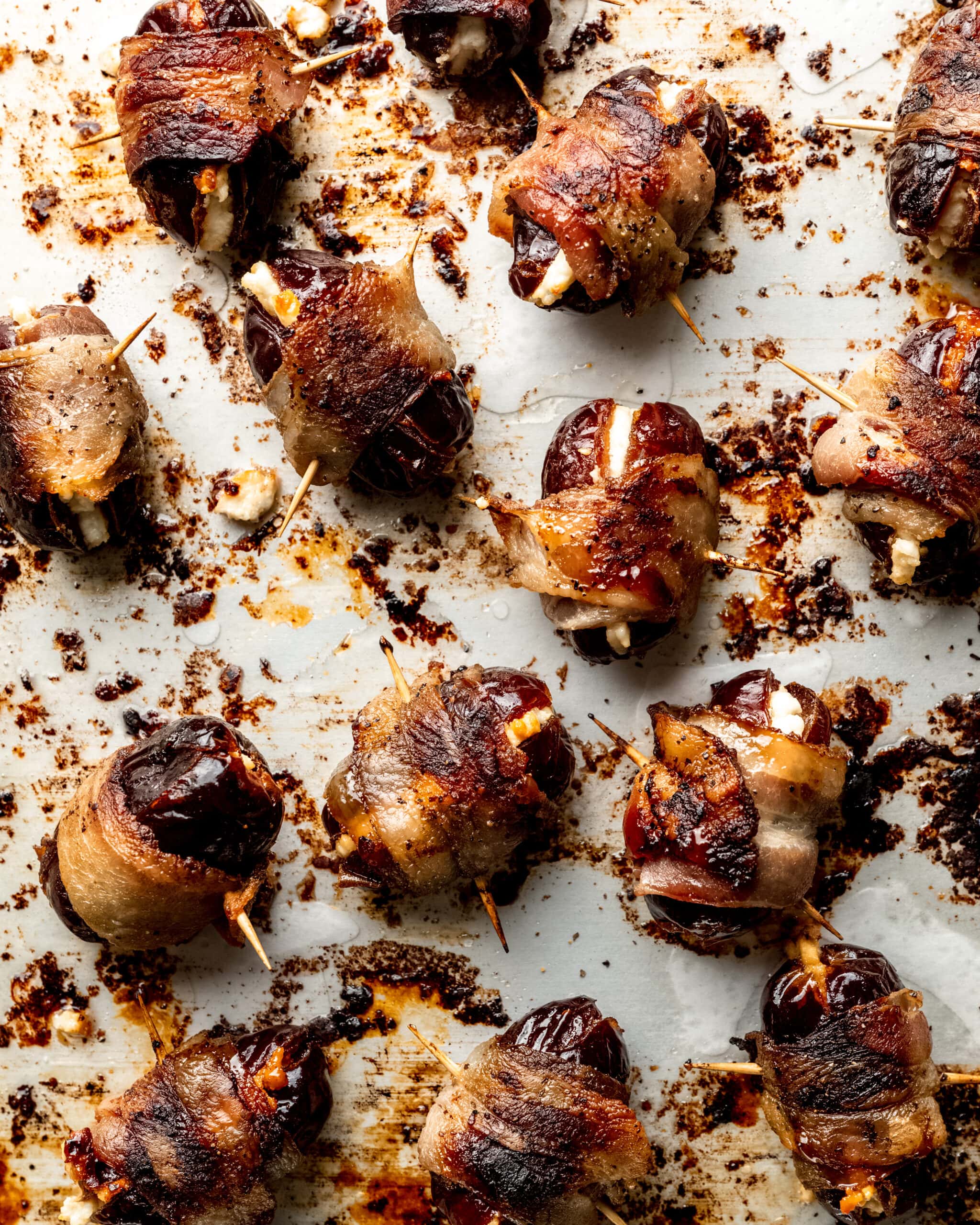 Bacon wrapped dates on a baking sheet with toothpicks securing them together.