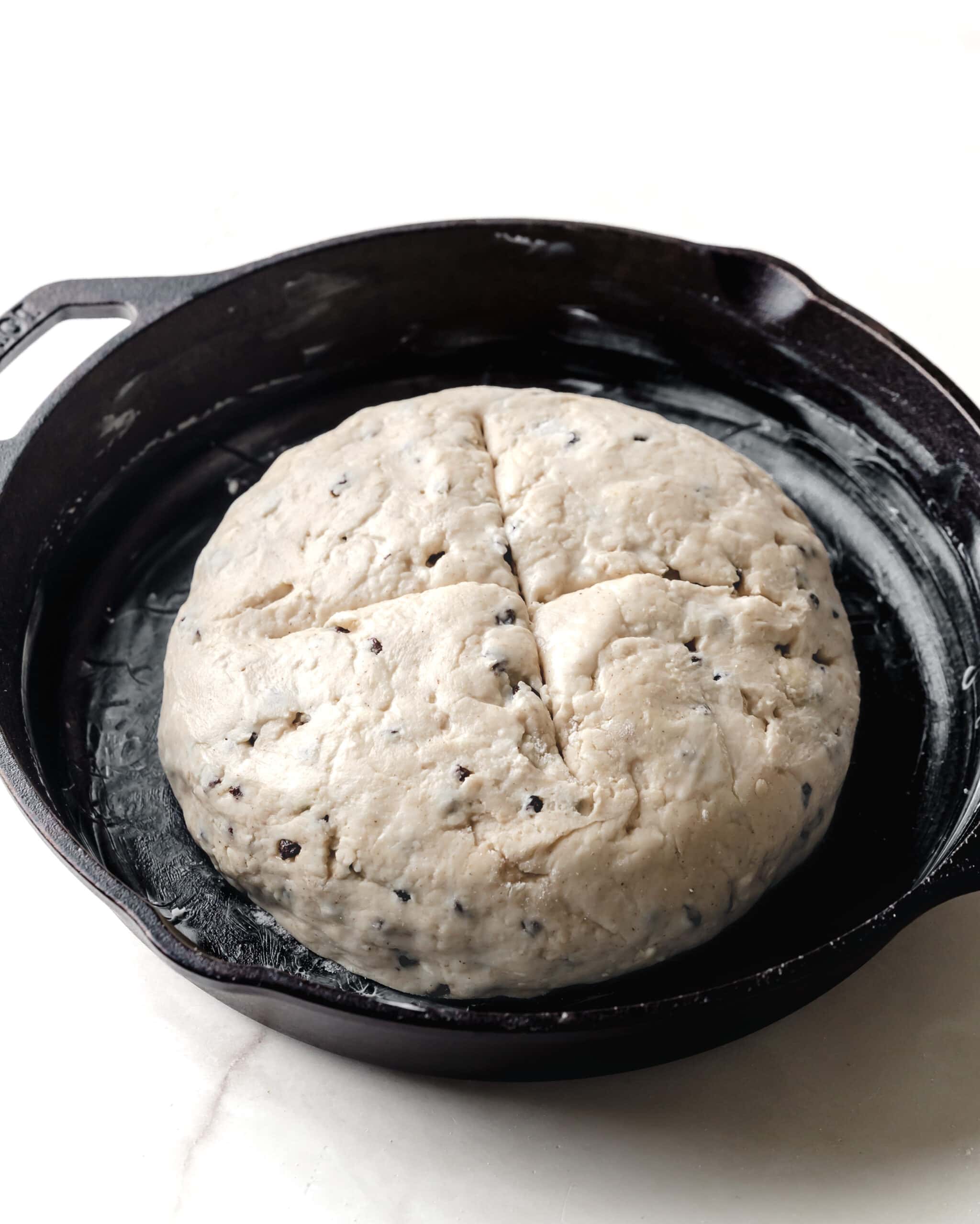 A round mound of soda bread in a greased cast iron skillet.