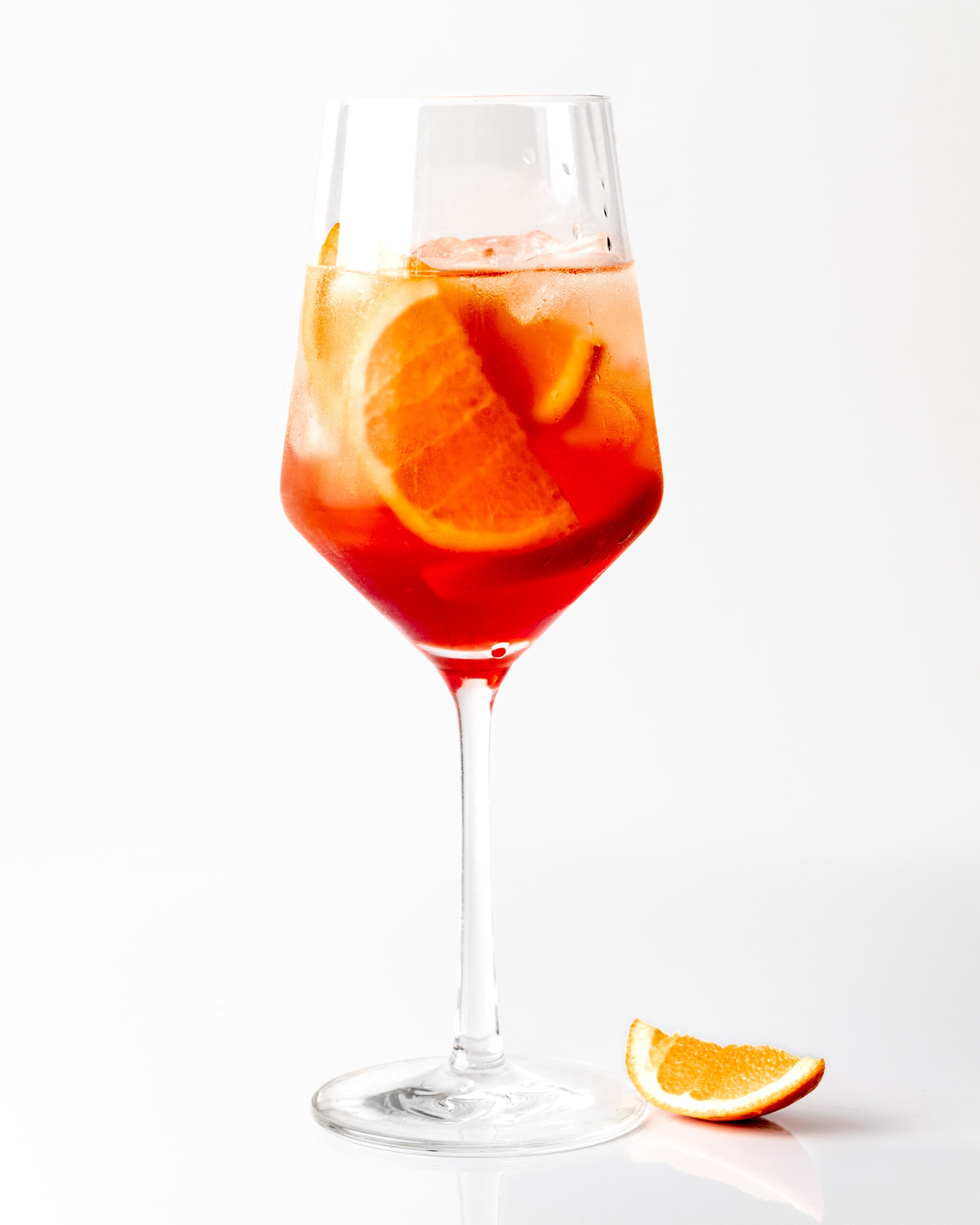 A photo of an Aperol Spritz drink in a glass, with a slice of orange on sitting next to it.