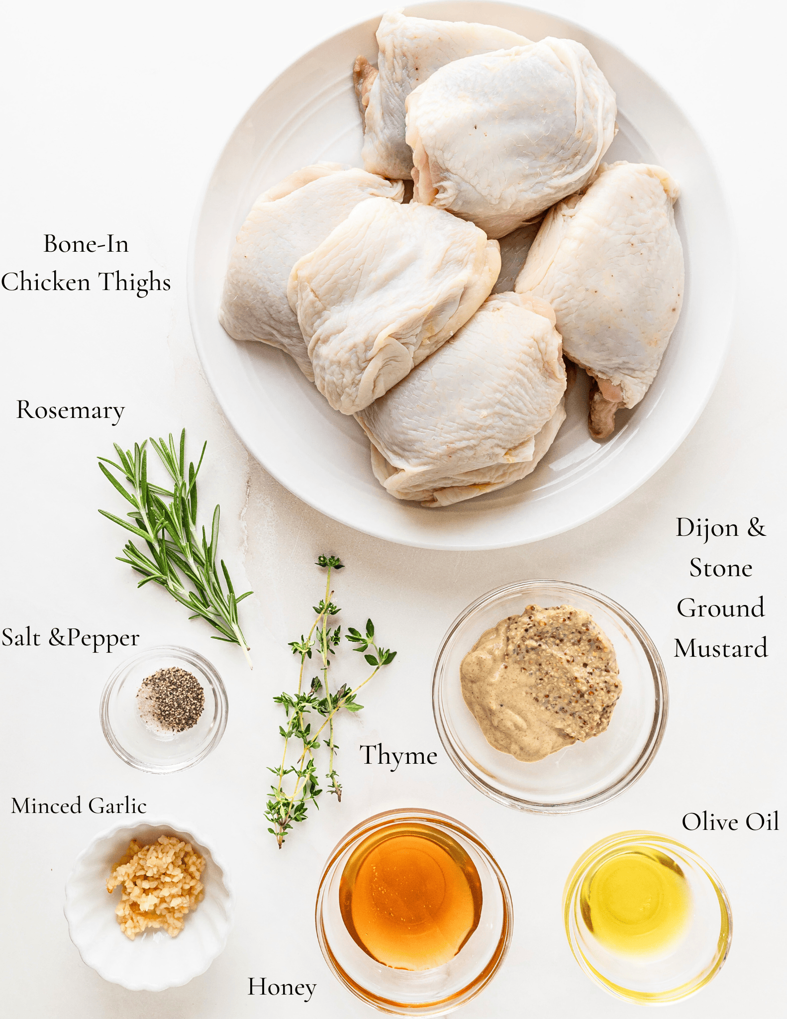 Ingredients for dijon mustard chicken. A plate of bone-in chicken thighs next to fresh thyme, rosemary, dijon mustard, stone ground mustard, salt, pepper, olive oil, honey, and minced garlic. 