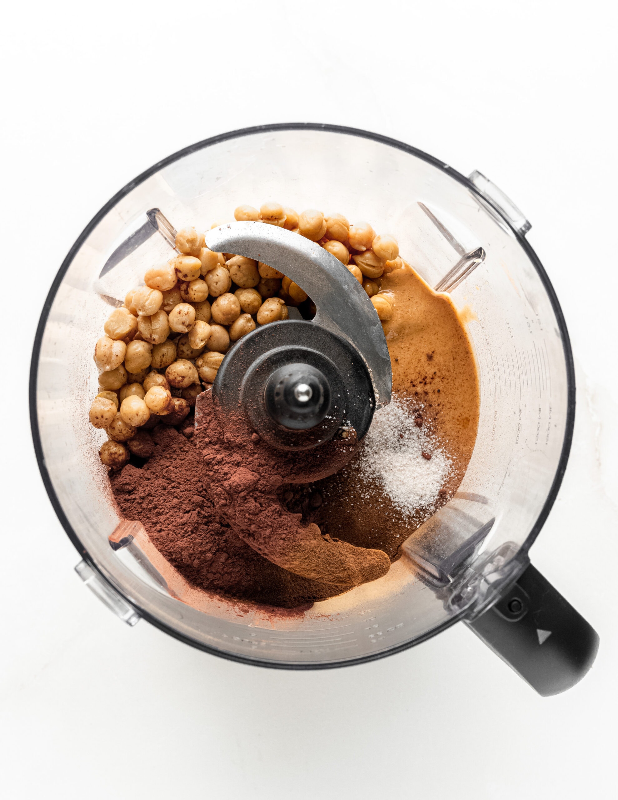 A food processor over head shot with garbanzo beans, cocoa powder, espresso powder, salt, and peanut butter. 