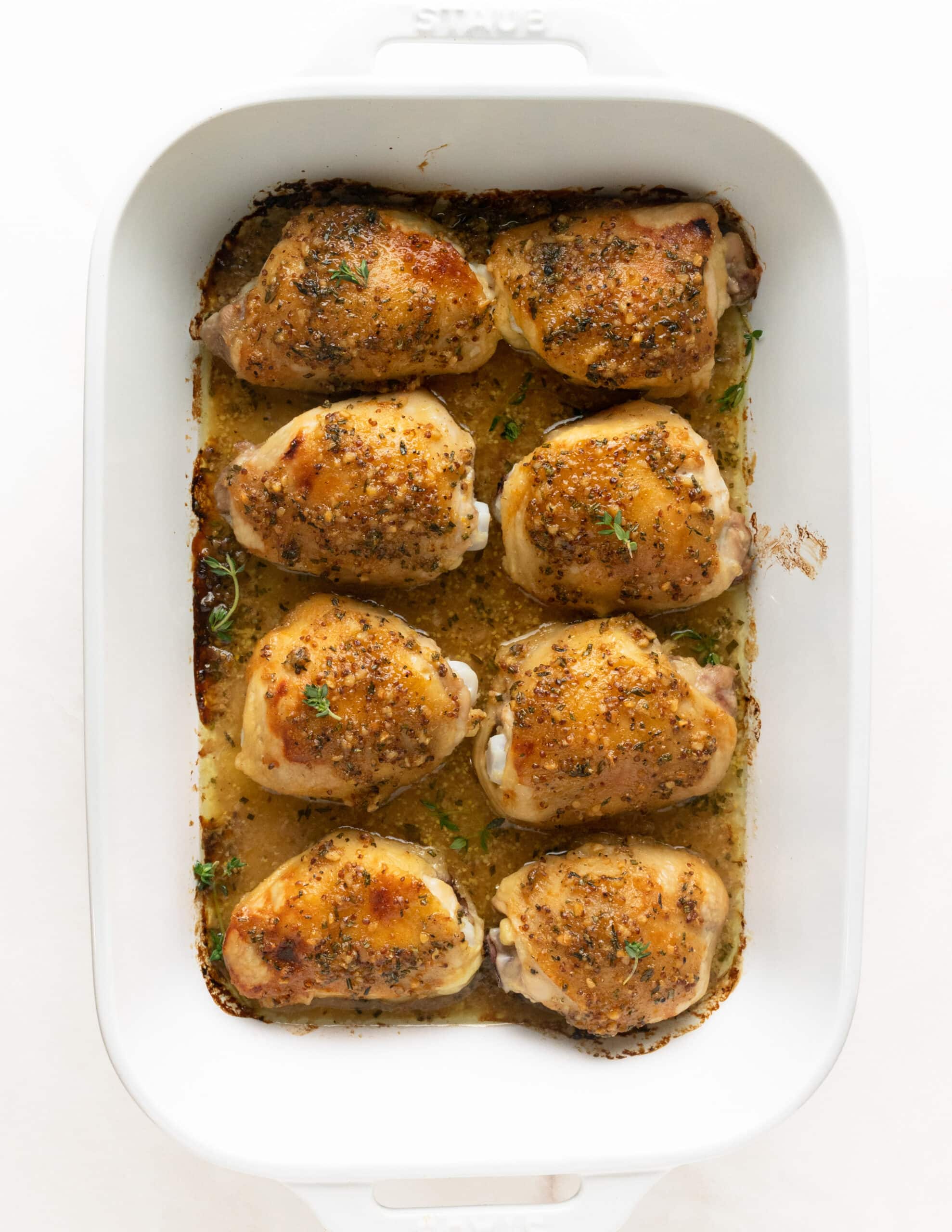 A large white ceramic baking dish of 8 fully cooked, bone-in chicken thighs with a honey dijon mustard sauce.