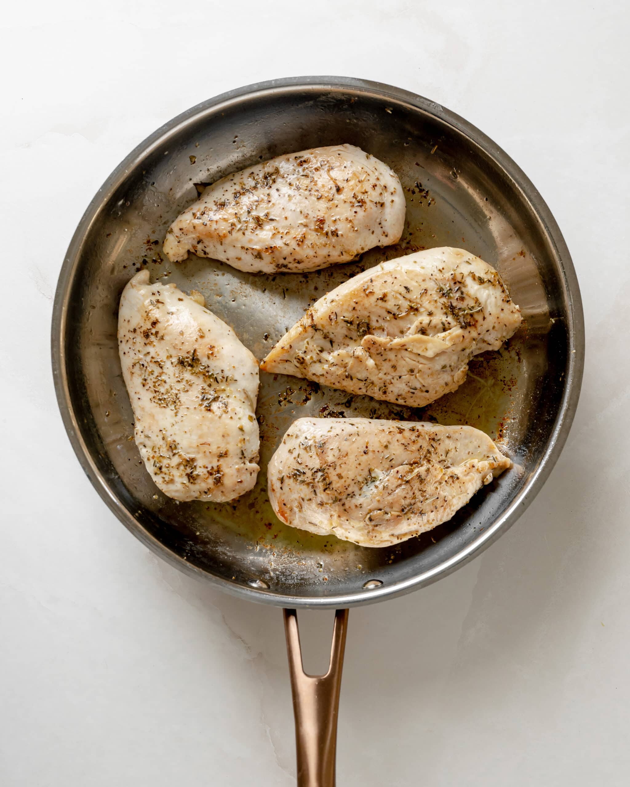 A large frying pan with a gold handle, searing 4 chicken breasts until golden brown. 