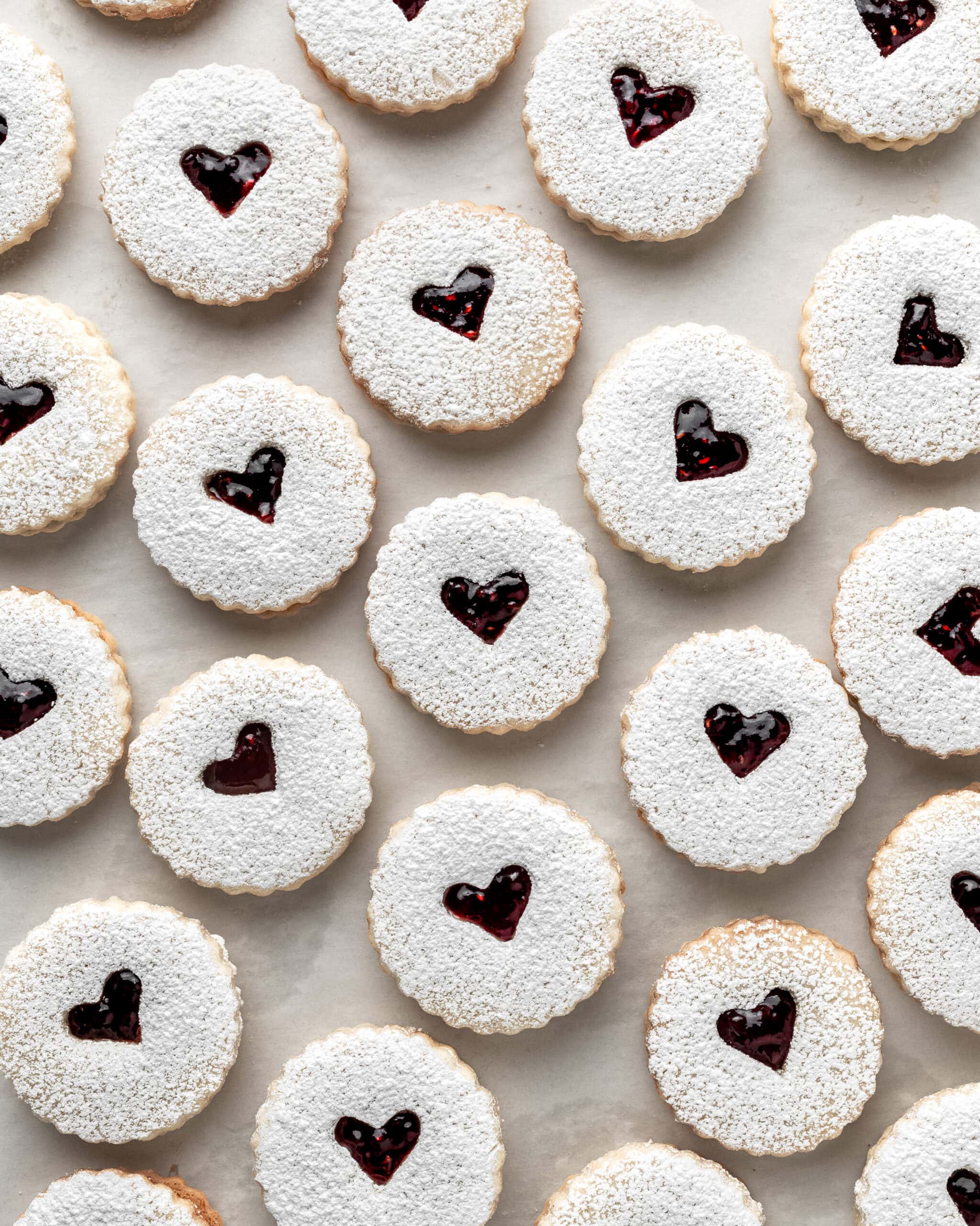 Gluten-free raspberry linzer cookies. Jam filled cookie with a heart in the middle exposing the red jam color, and powdered sugar on top.
