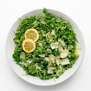 Arugula (Rocket Salad) in a white bowl with cheese and lemons.
