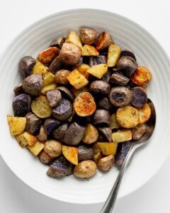 Rainbow potatoes in serving bowl with spoon and fresh rosemary.