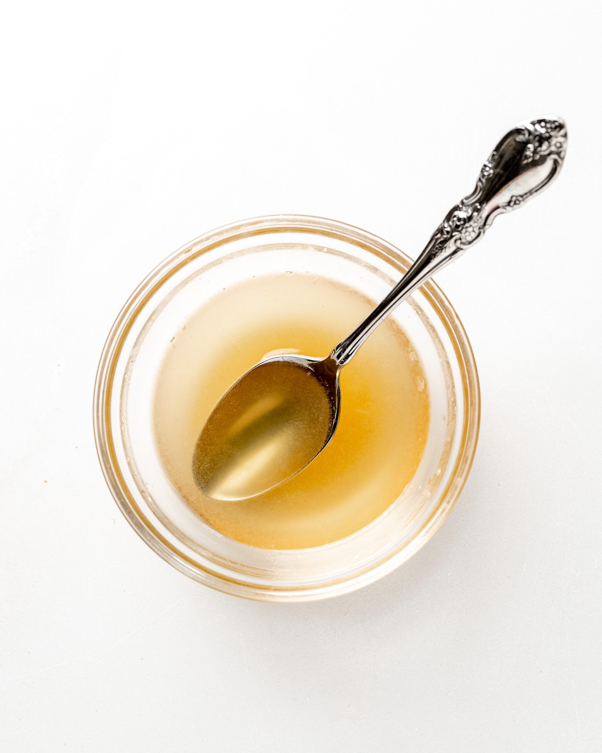 A clear glass bowl with a honey lemon syrup and a silver spoon in the middle.