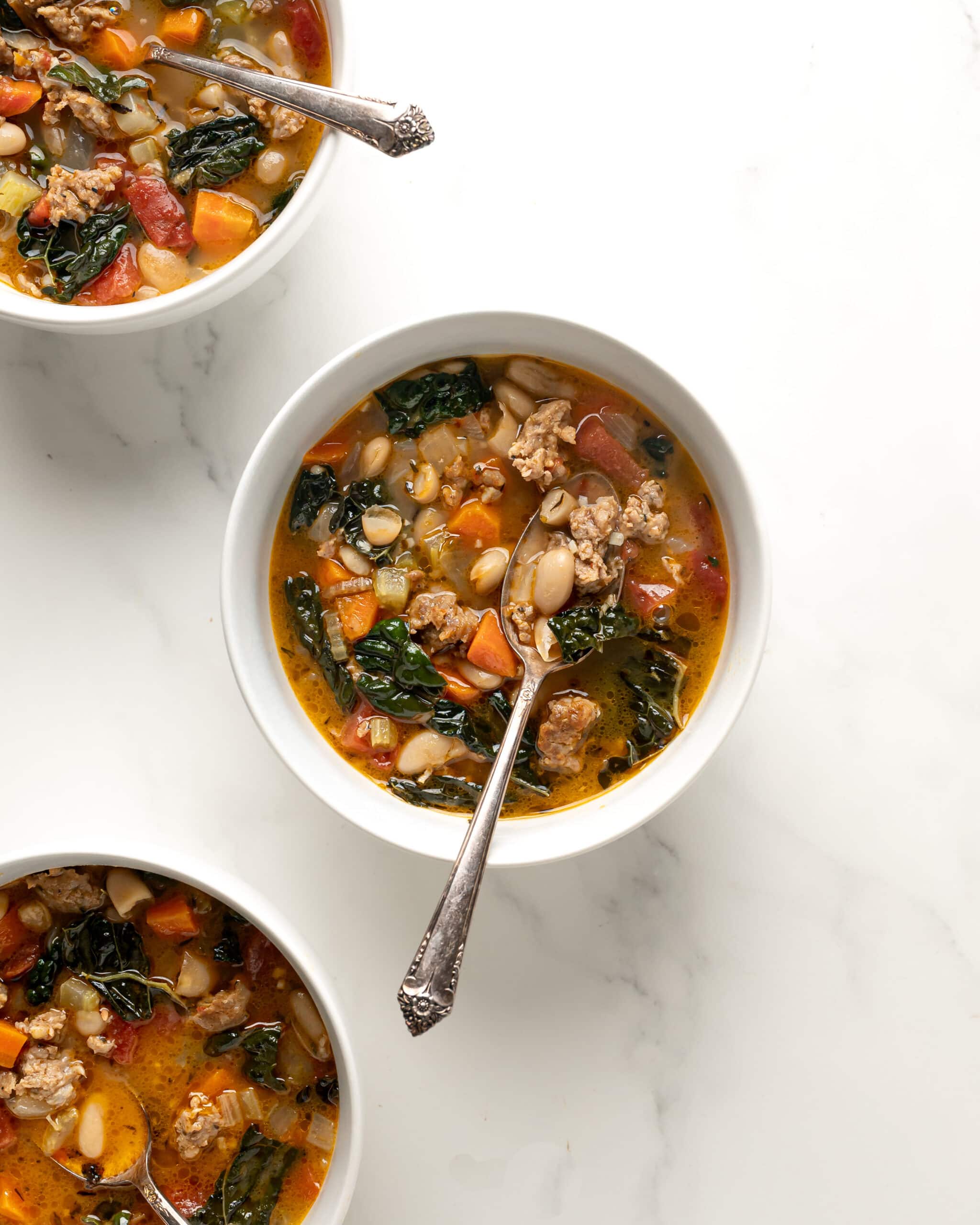 Three white bowls filled with tuscan kale soup with silver spoons in the middle.
