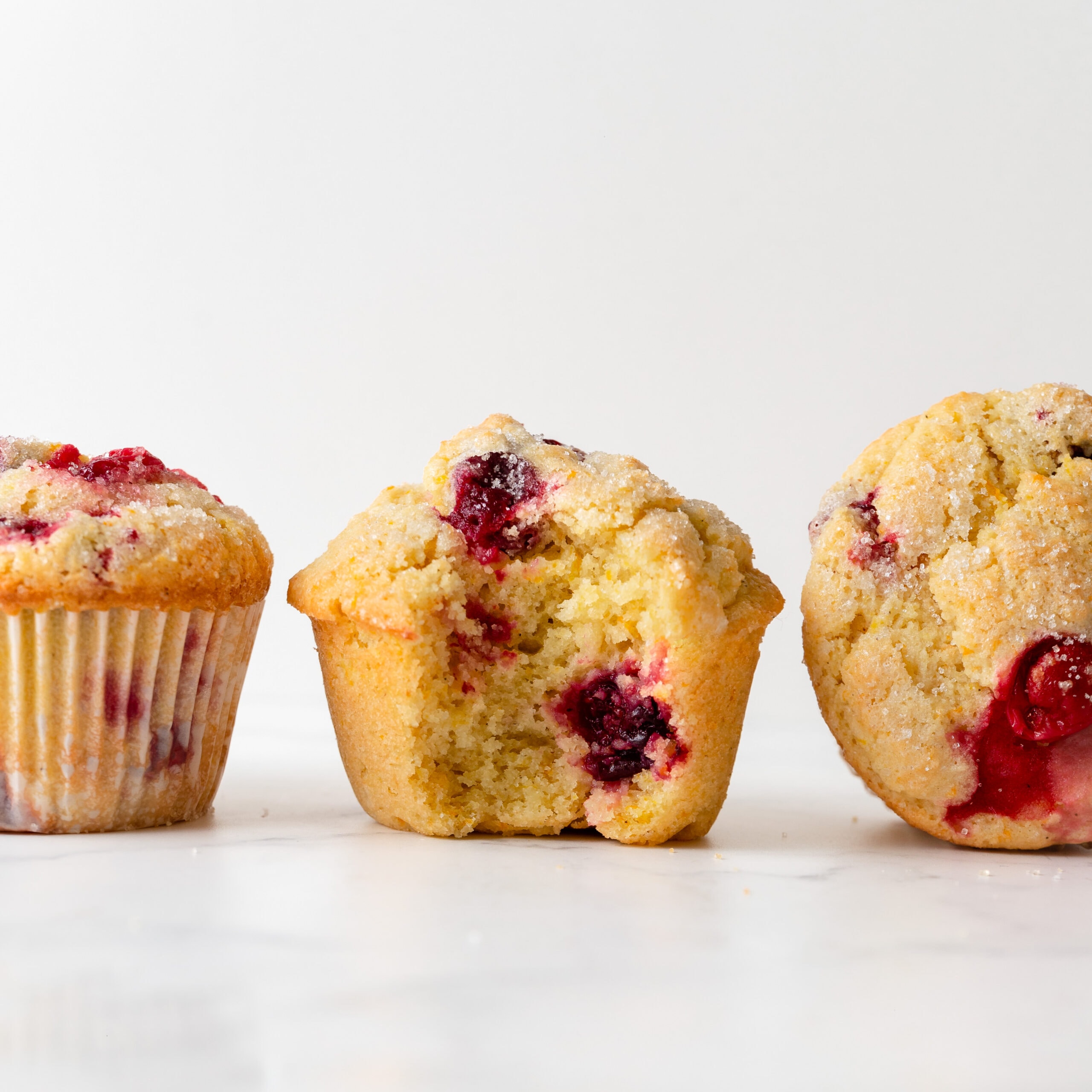 Three cranberry orange muffins, one with a bite take out of the middle showing the crumb and cranberries.