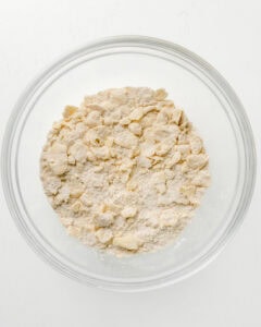 Pie dough with large cubes of butter in a clear bowl.