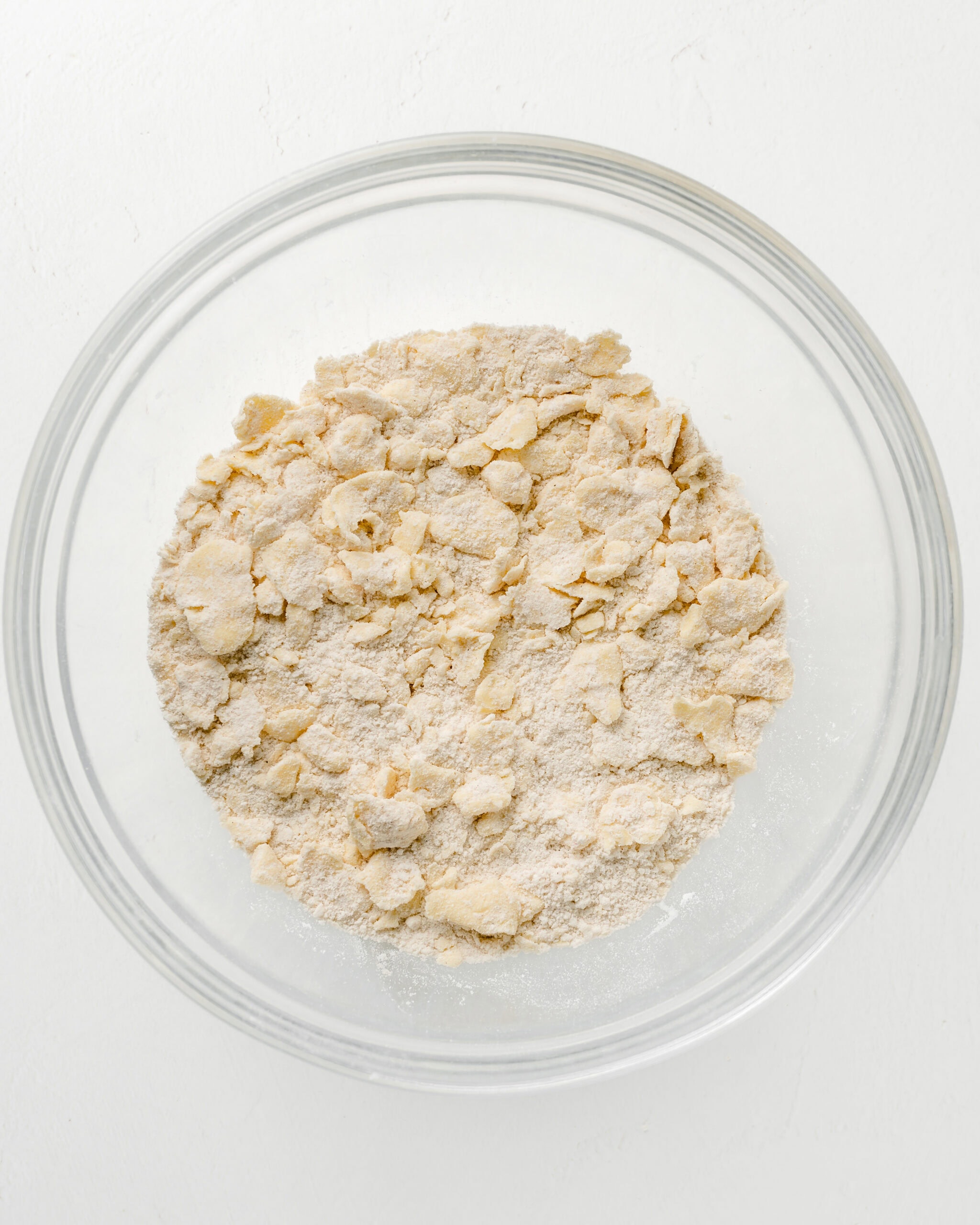 Pie dough with large cubes of butter in a clear bowl.
