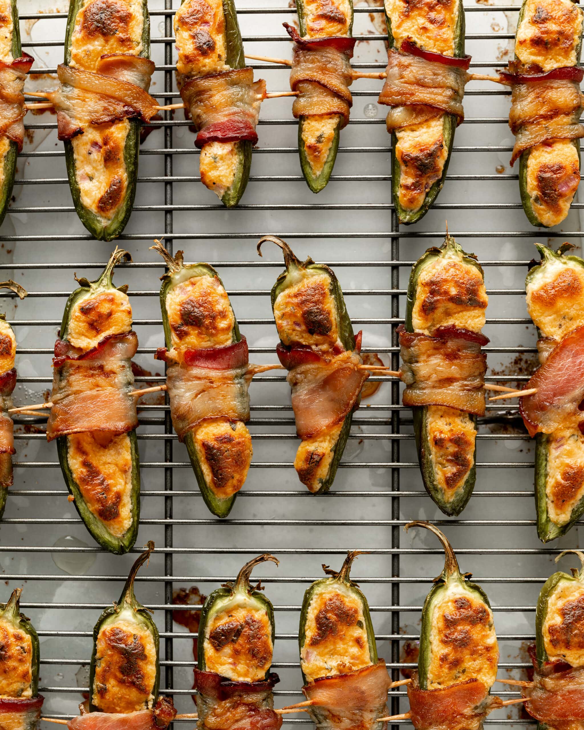 A close up photo of bacon wrapped jalapeno poppers on a wire rack.