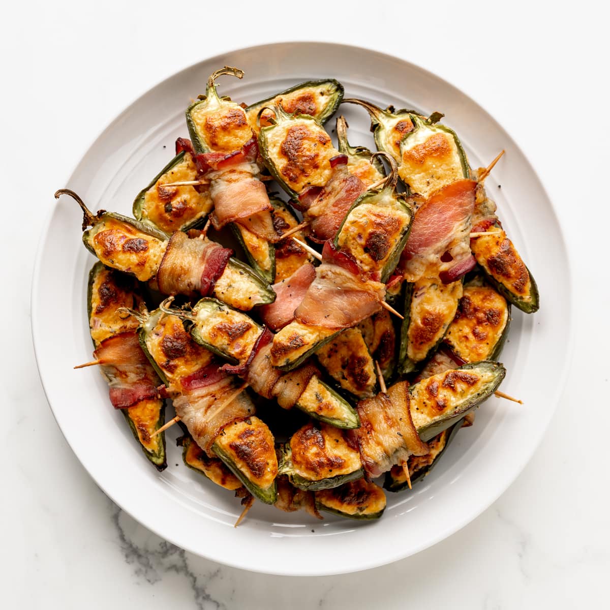 A round white plate with low carb jalapeno poppers wrapped in bacon, stacked on top of one another. 