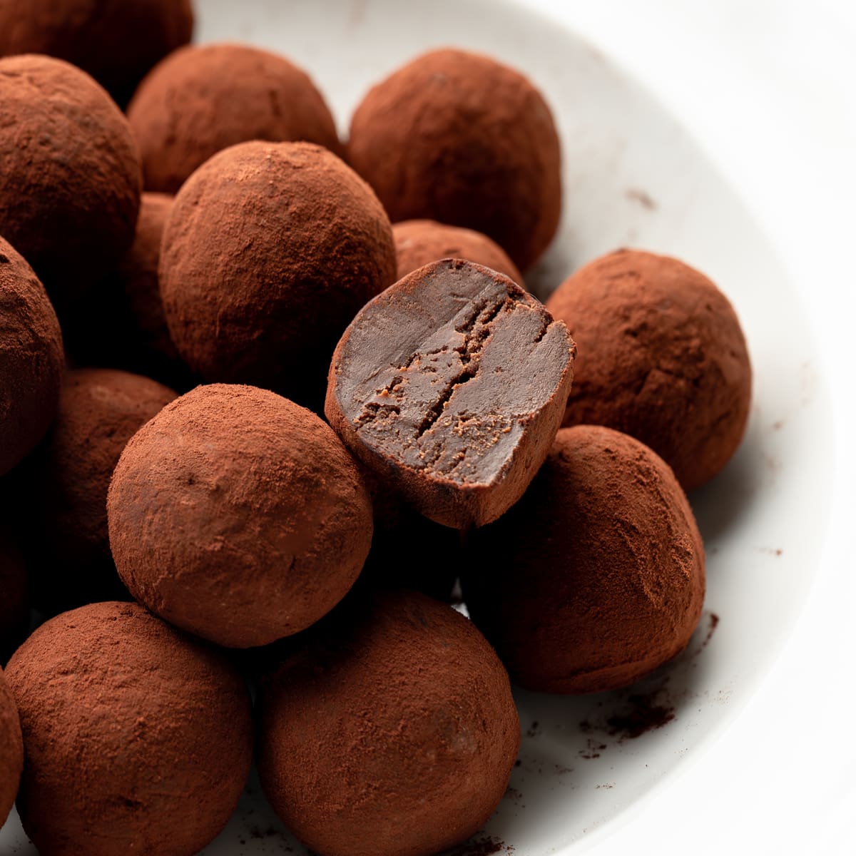 A bowl of cocoa dusted French truffles with one truffle cut in half exposing the fudgy center. 