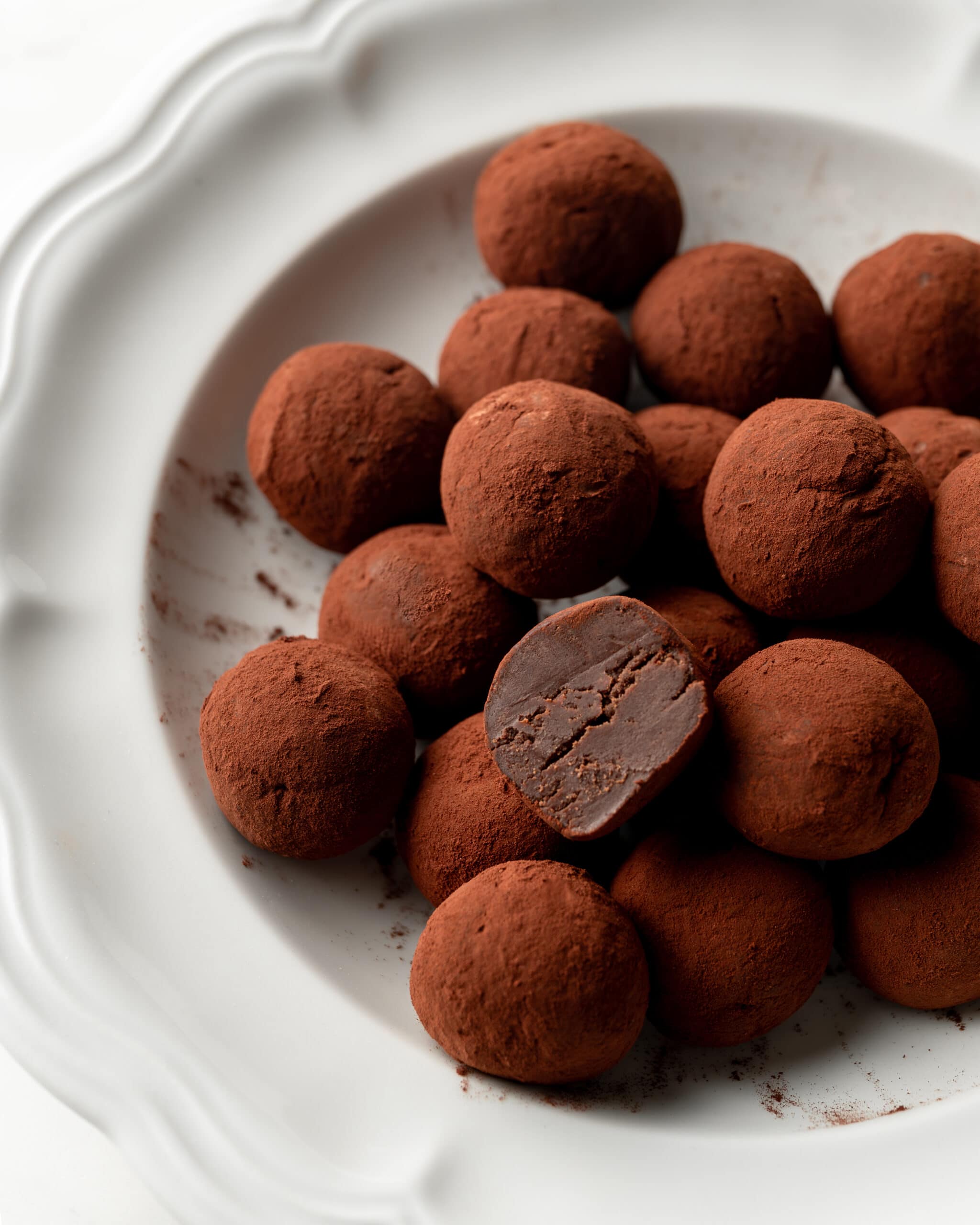 French truffles coated in cocoa powder with one truffle cut in half exposing the inside. 