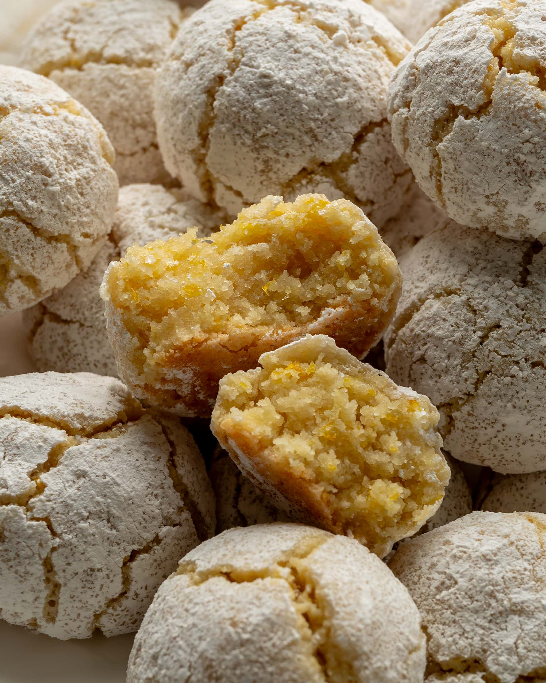 Limoncello cookies cut in half with a zesty lemon colored filled exposed. The tops of the cookies are coated in  white powdered sugar.