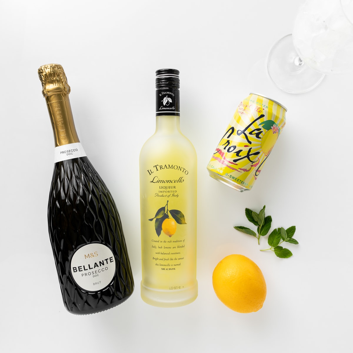 Ingredients for limoncello spritz. Bottle of prosecco, limoncello liqueur, Lax Croix sparkling water, fresh lemon and two sprigs of mint.  