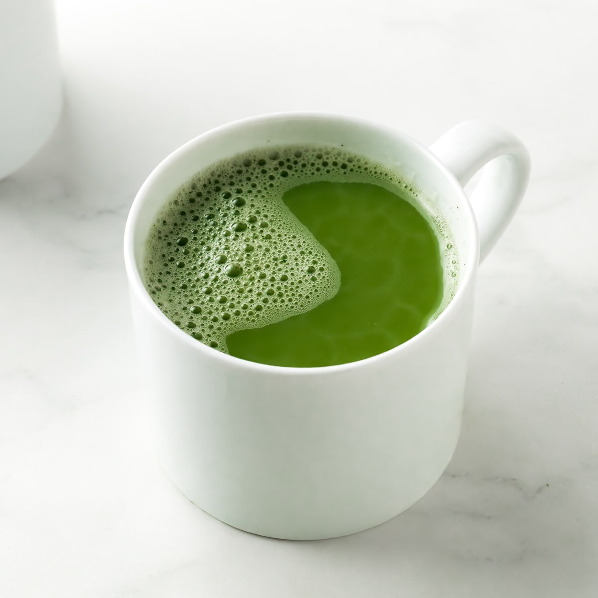 A white ceramic cup with vanilla matcha latte. Bubble are forming at the top of the cup with a vibrant green color showing through. 