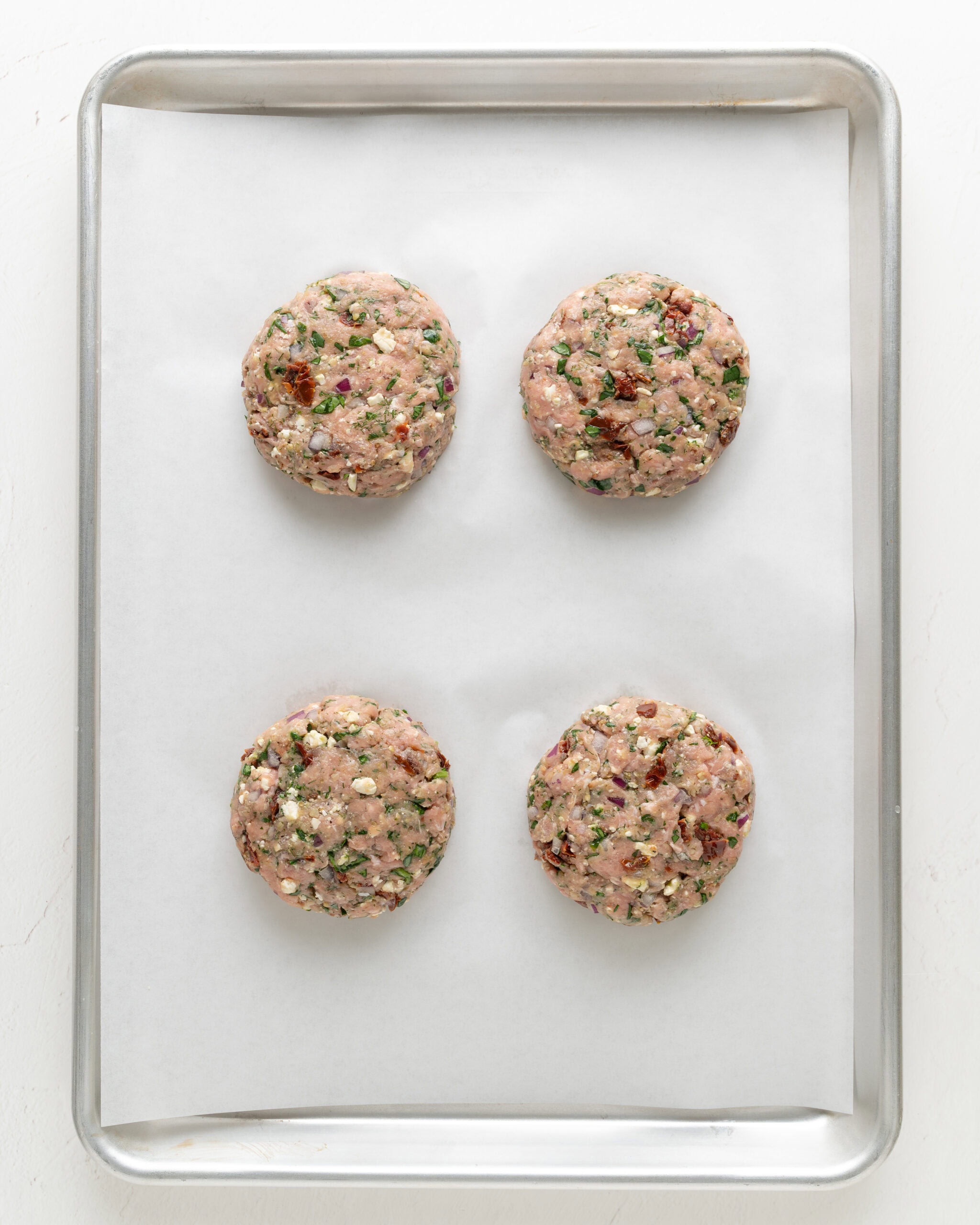 feta and spinach turkey burgers patties on a lined baking sheet.