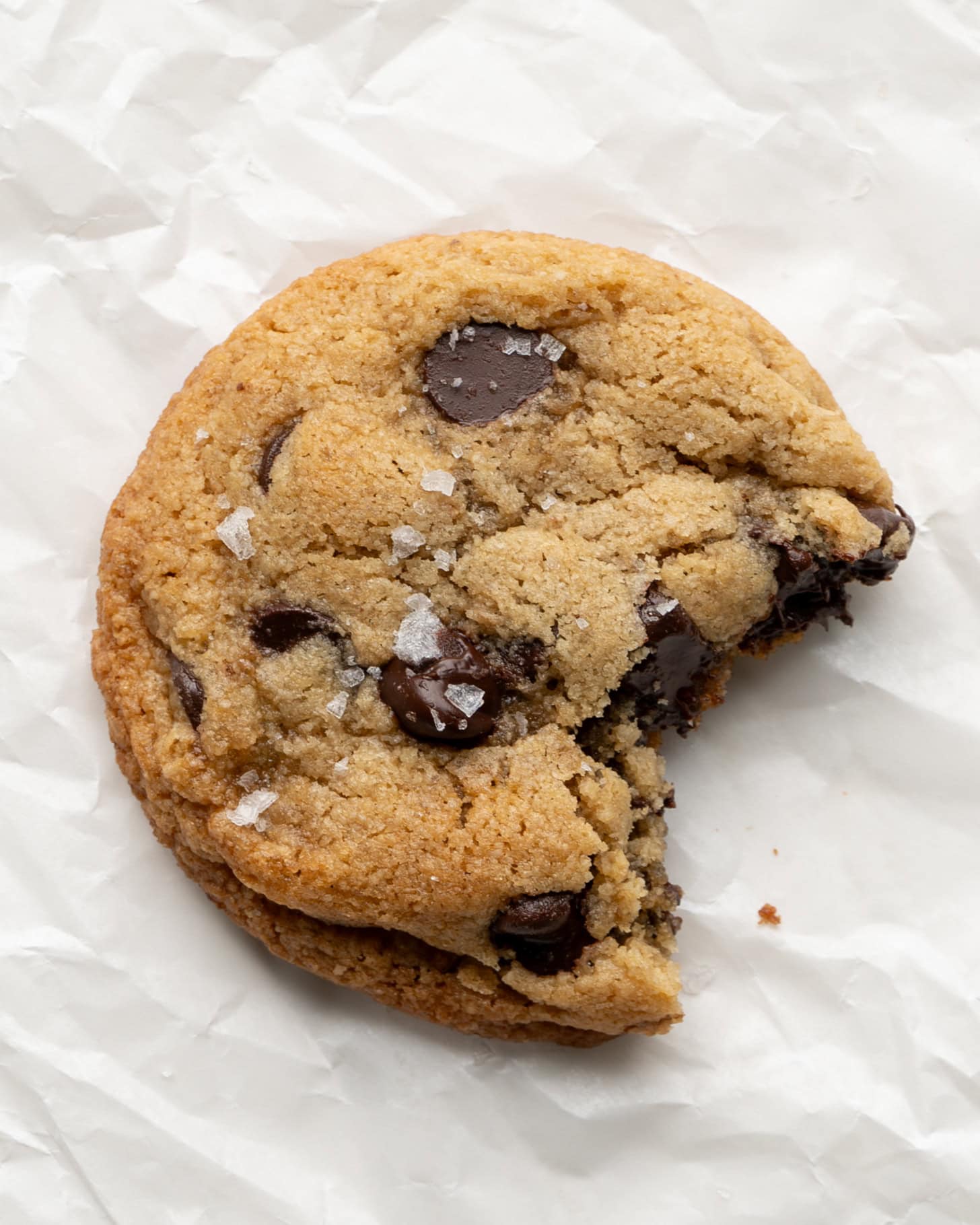 Almond flour chocolate chip cookies with a bite taken out and flaky sea salt on top.