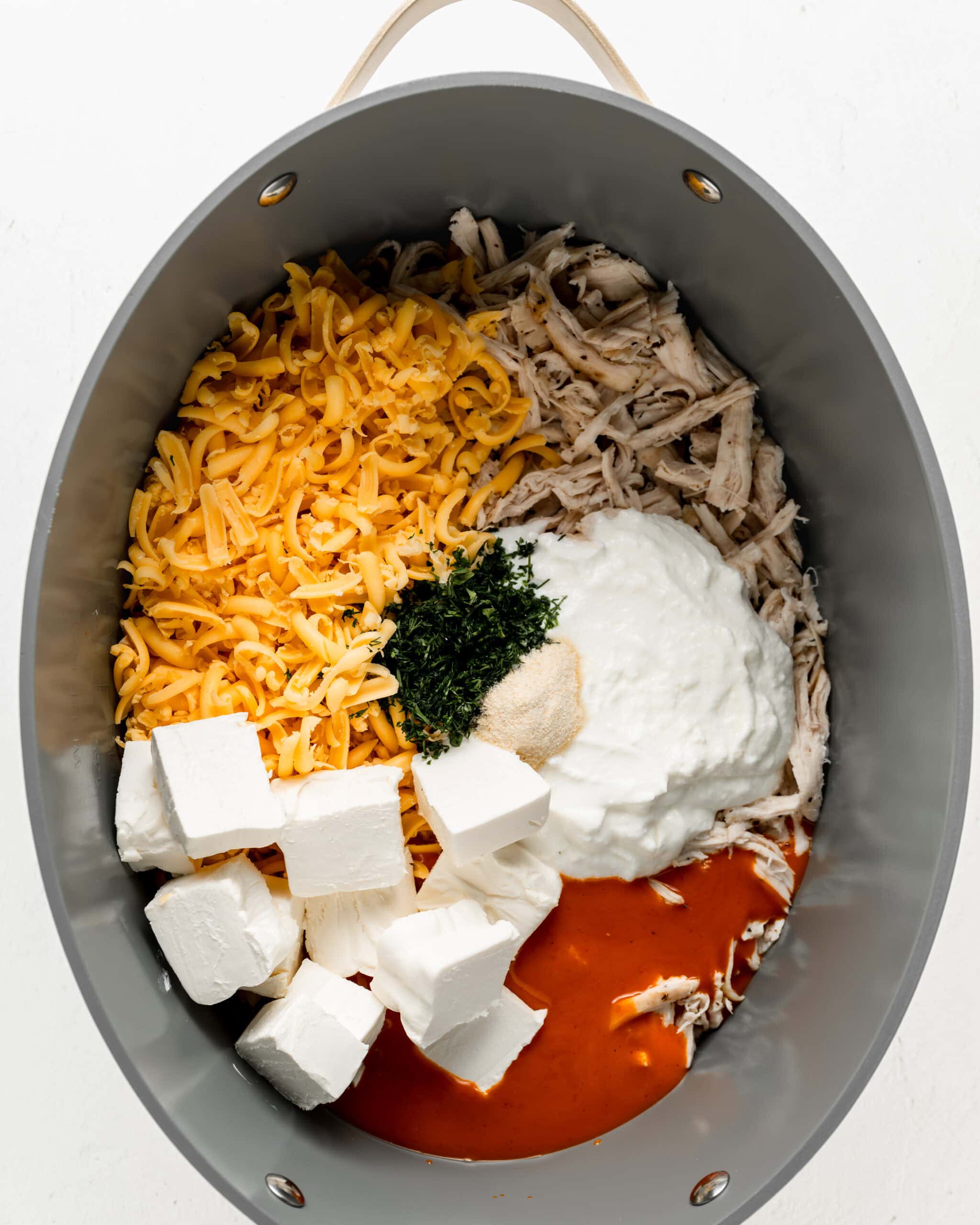 Adding all ingredients to crockpot for buffalo chicken dip.