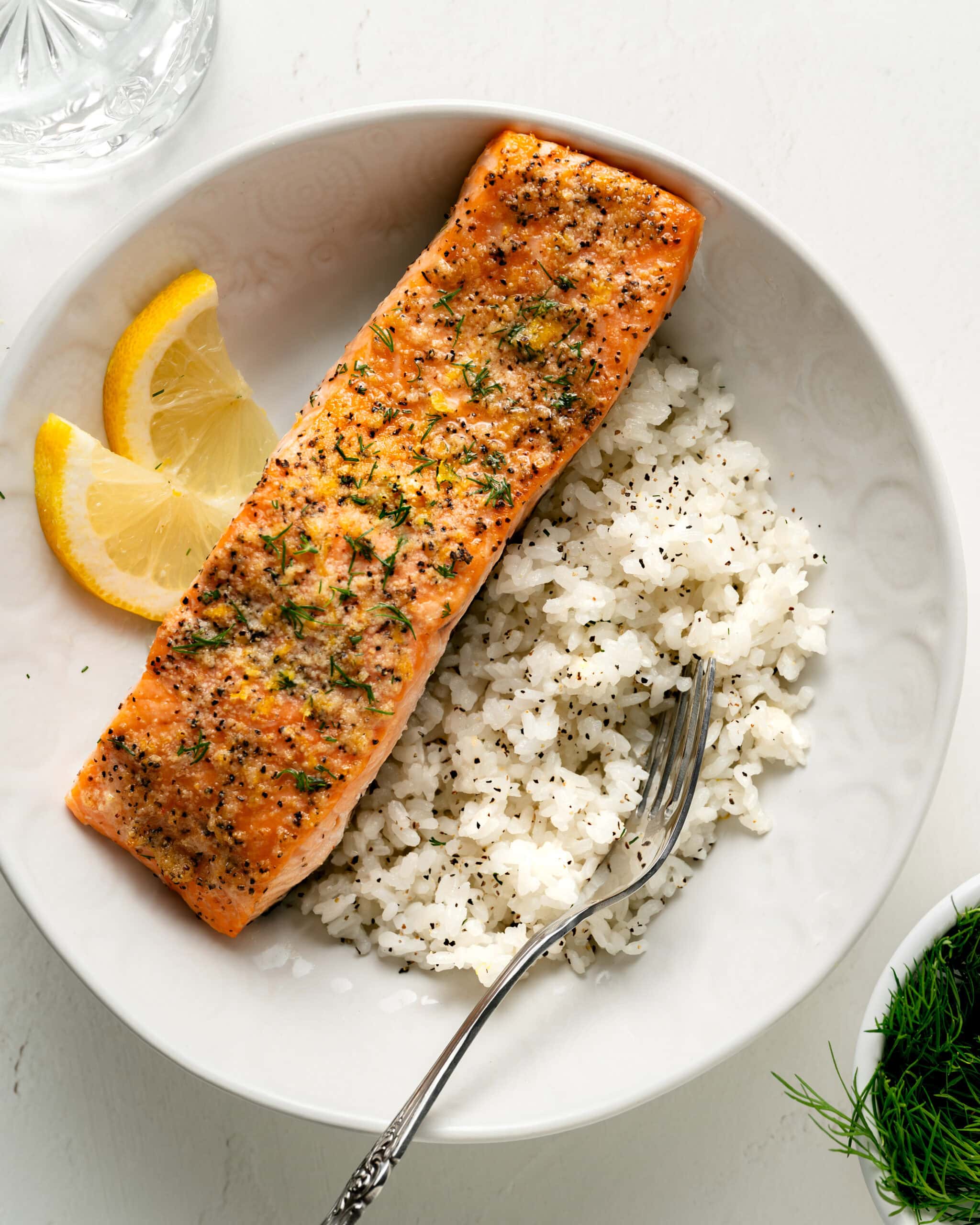 Garlic Butter Dill Salmon in a large white bowl with lemon slices and white rice, garnished with freshly chopped dill.